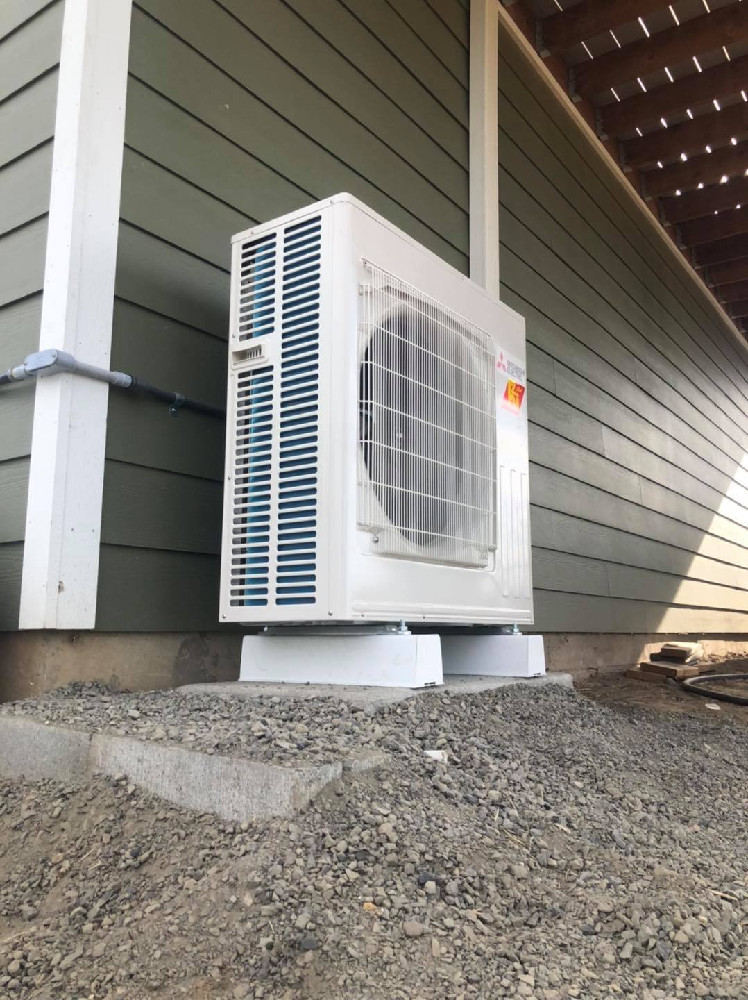 Outdoor air conditioning unit installed on concrete blocks beside the house wall with gray siding.