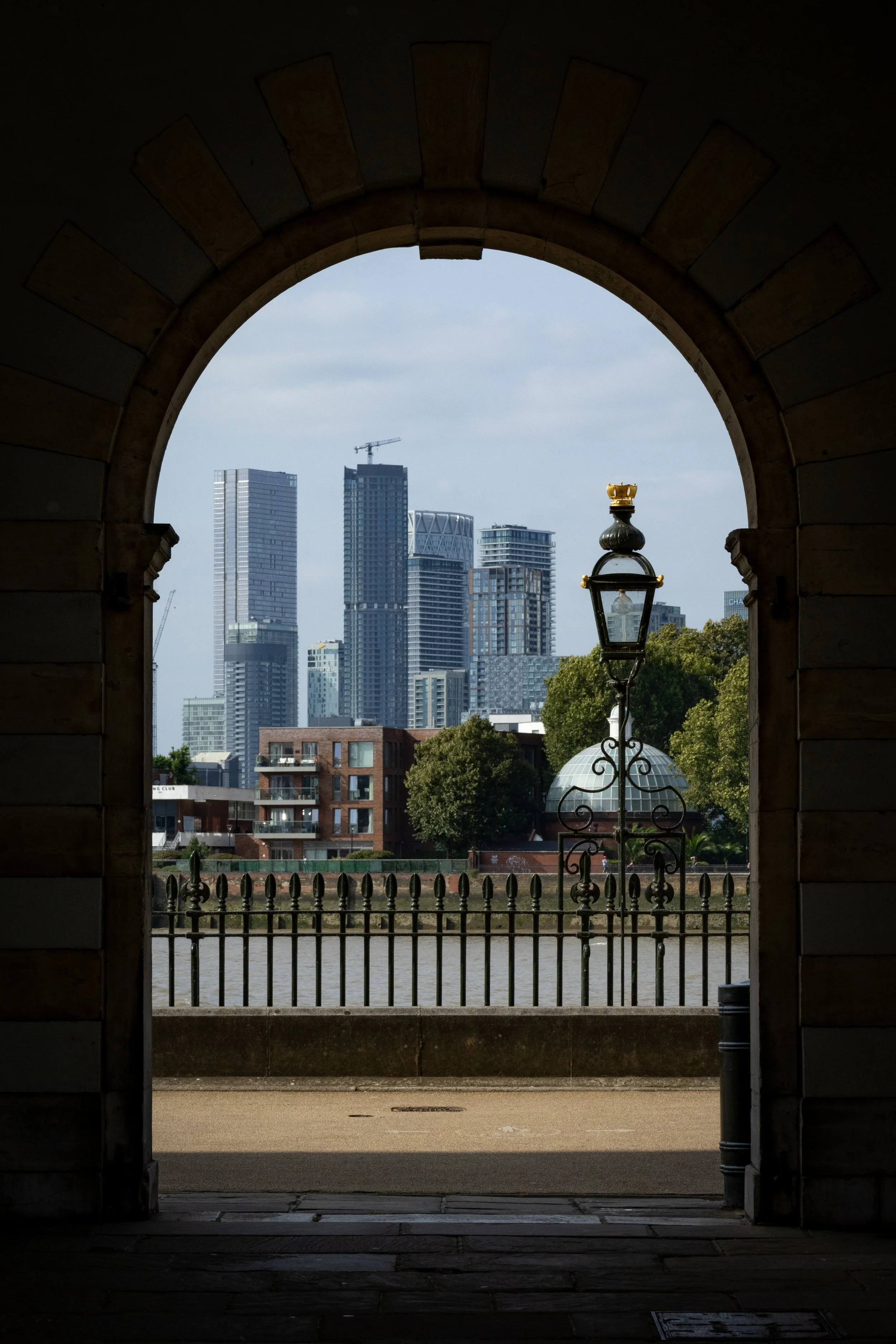 View of a city skyline with modern skyscrapers seen through an archway with a lantern and railing in the foreground.