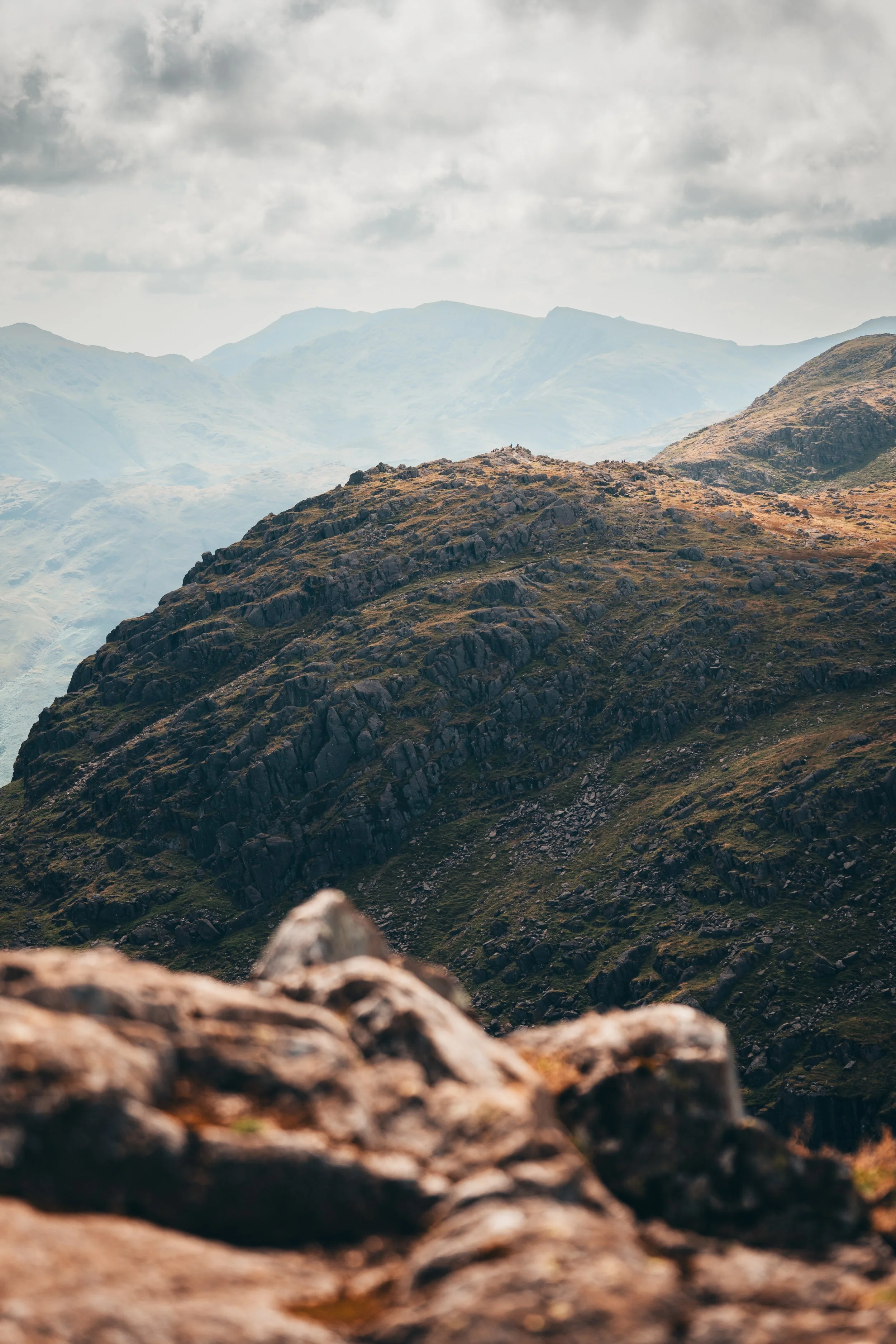 Mountain landscape with rocky terrain, green slopes, and cloudy sky.