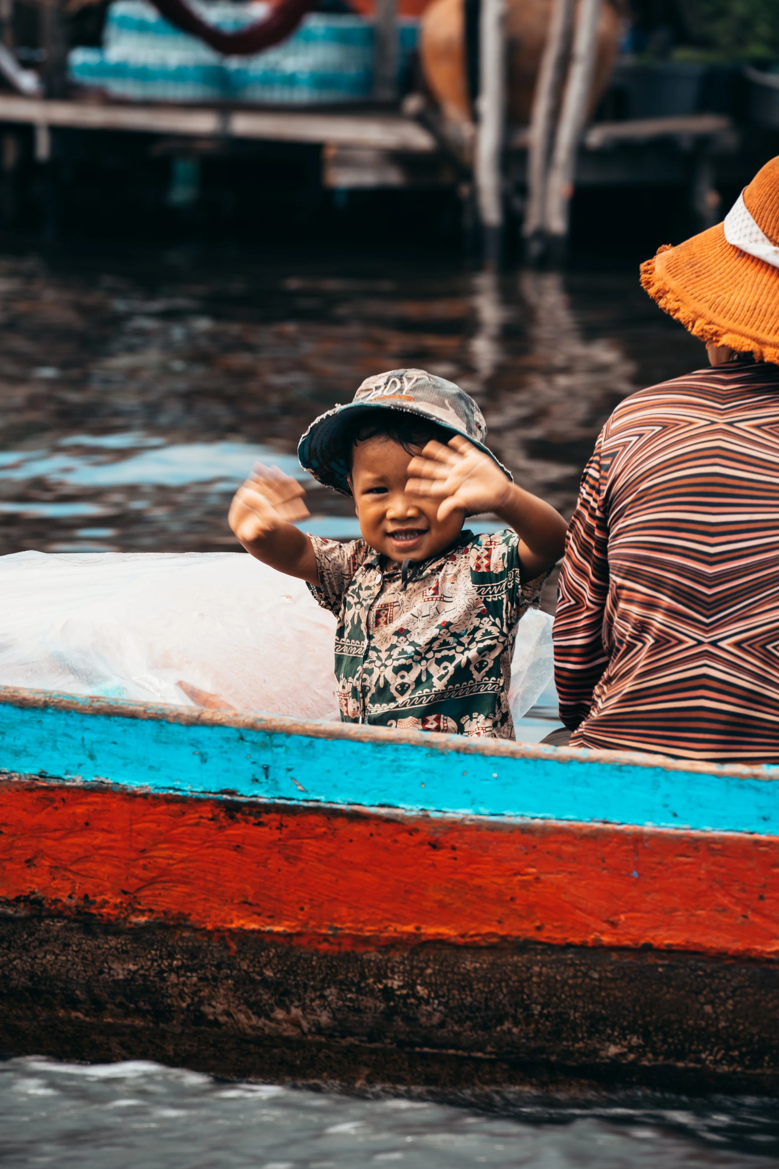 A small child waving while their mother rows a boat home in Kompong Phluk, Cambodia