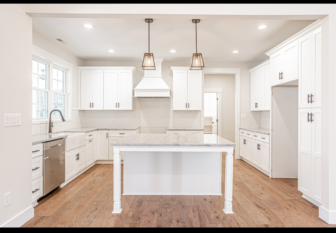 Modern white kitchen with island, wooden flooring, white cabinets, two pendant lights, and windows