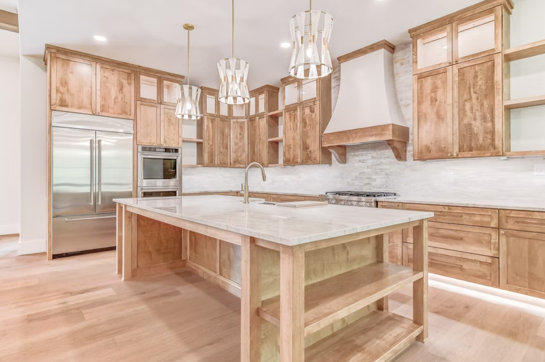 A modern kitchen with wooden cabinets, a kitchen island, stainless steel appliances, and pendant lights.