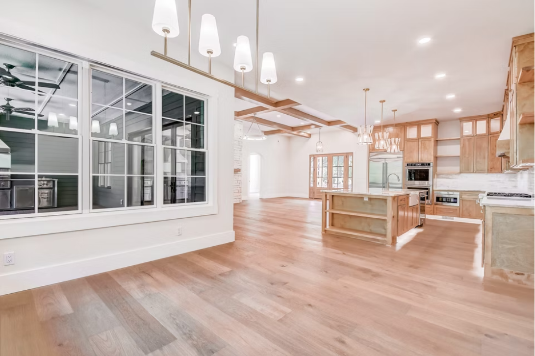 Open-concept kitchen and living area with wooden floors, kitchen island, light wood cabinetry, and large windows.
