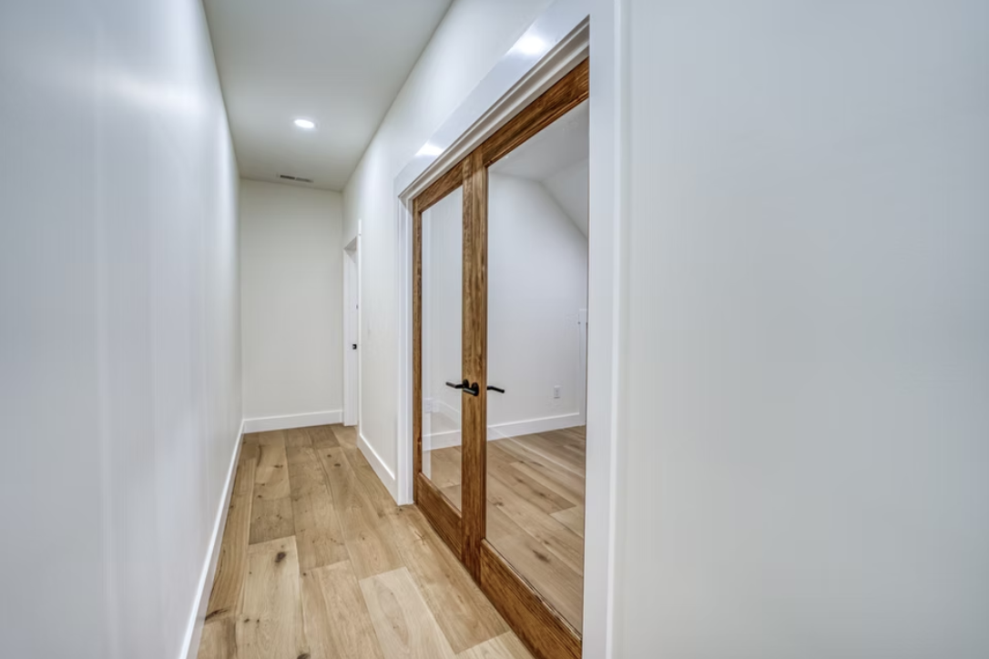 Empty hallway with white walls, wooden flooring, and a sliding glass door with wooden frame.