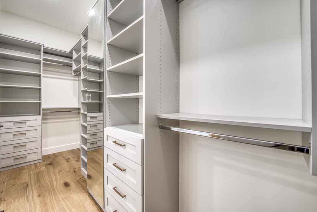 Empty walk-in closet with white built-in shelving, drawers, and wooden flooring.