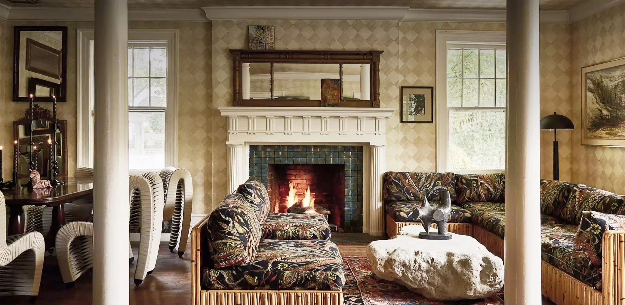 Living room with a fireplace, floral upholstered furniture, a rock coffee table, and large windows.