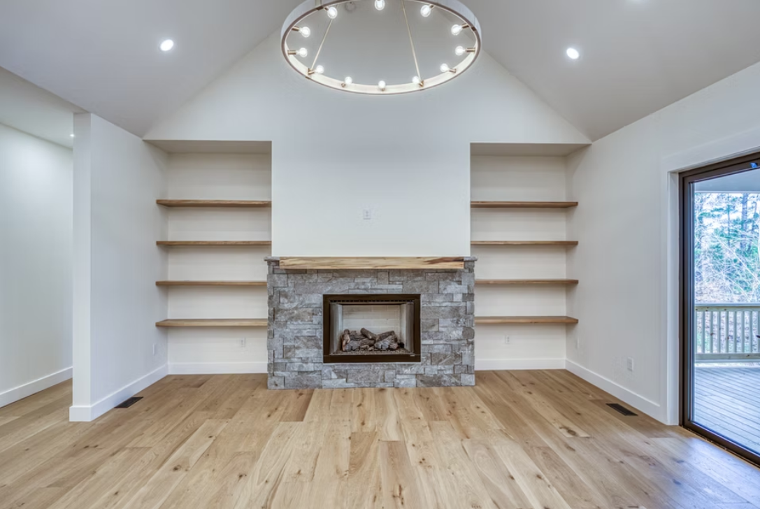 Living room with a stone fireplace, built-in shelves on each side, hardwood floors, and a sliding glass door leading outside.