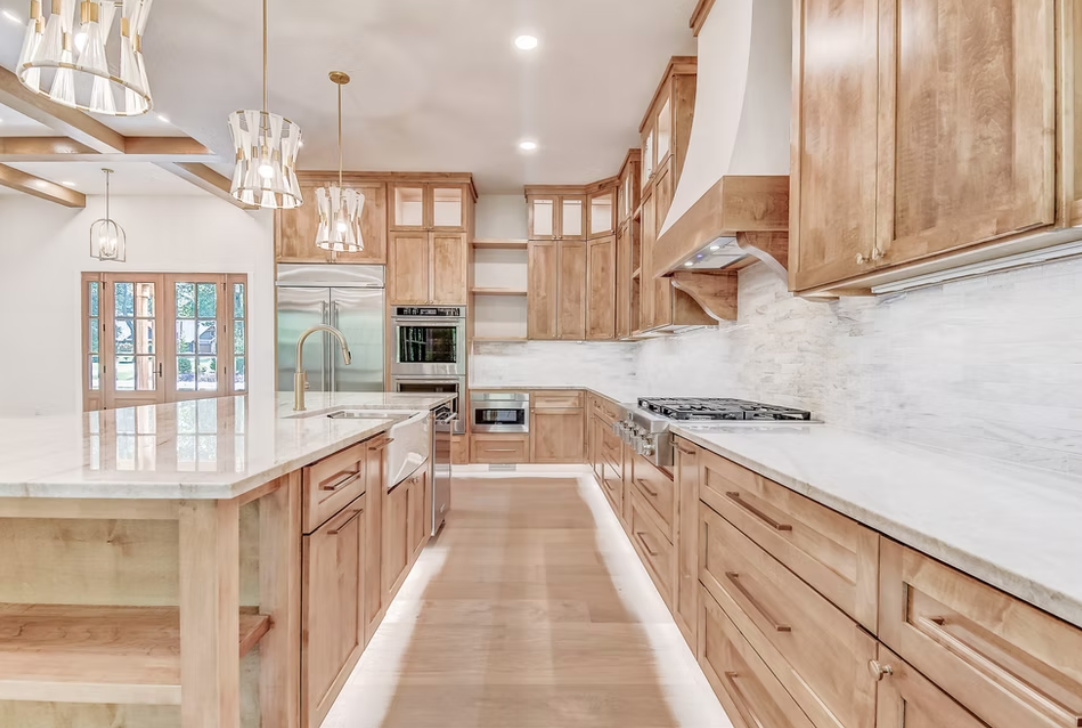 Modern kitchen with light wood cabinets, white marble countertops, stainless steel appliances, and pendant lighting.