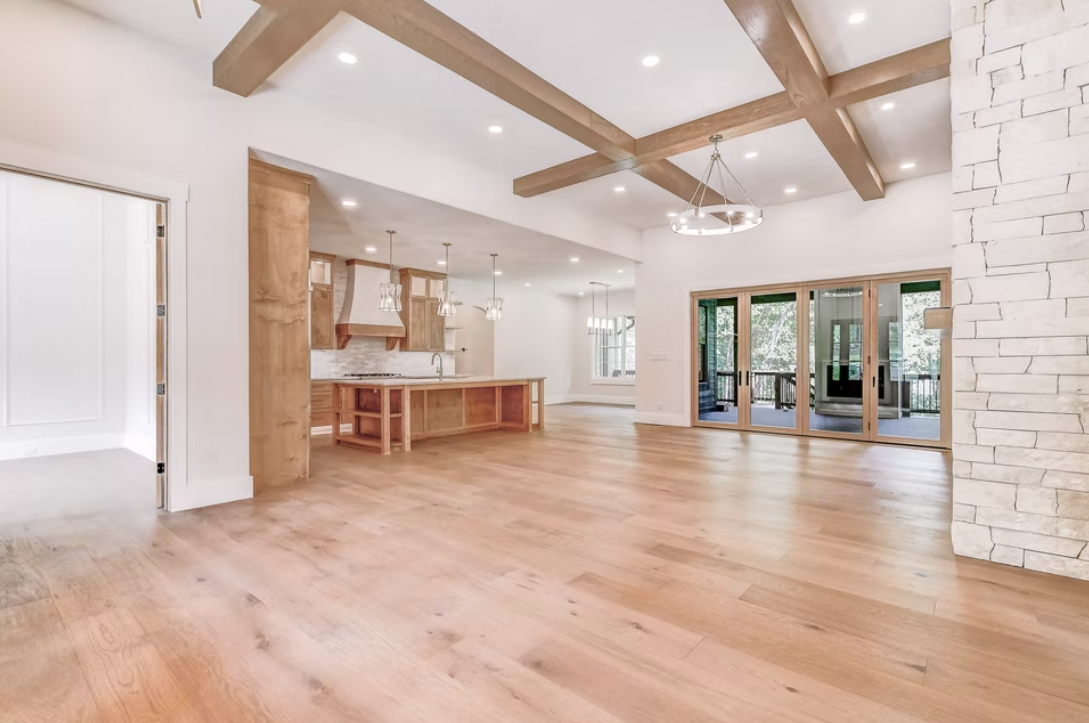 Open-concept living area with hardwood floors, a kitchen with an island, hanging pendant lights, and large sliding glass doors leading to a deck.