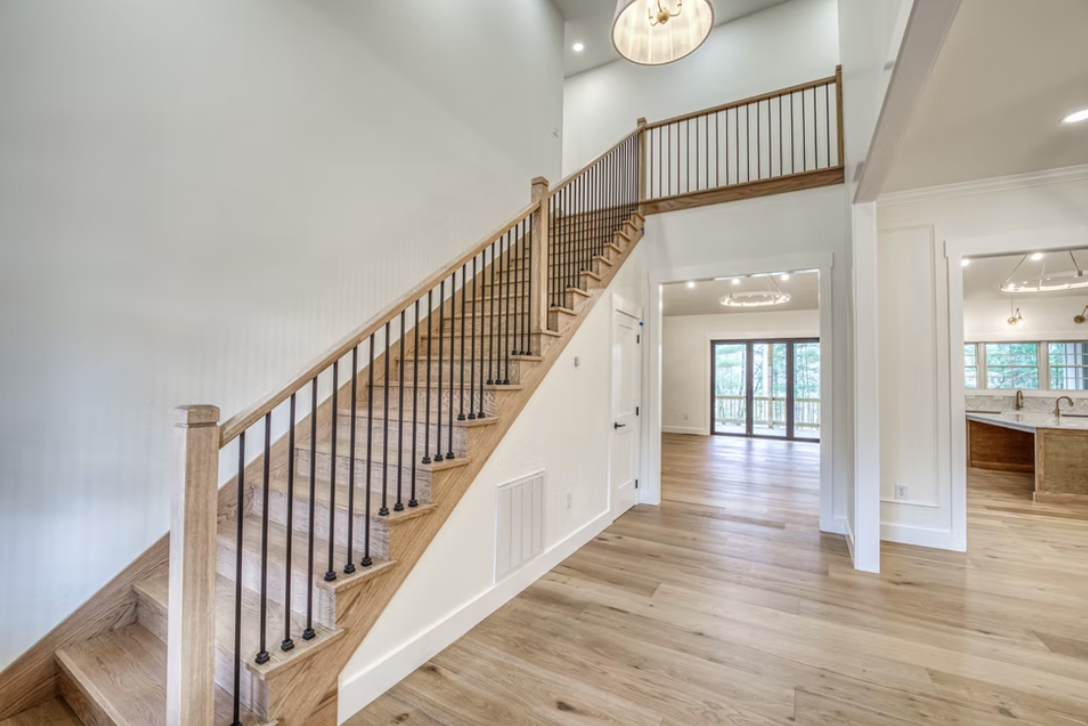 Interior of a modern house with a wooden staircase, open floor plan, hardwood floors, and sliding glass doors to a balcony.