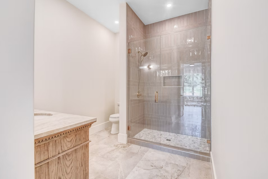 Bathroom with a walk-in shower with glass doors and beige tiles, a toilet, and a wooden vanity