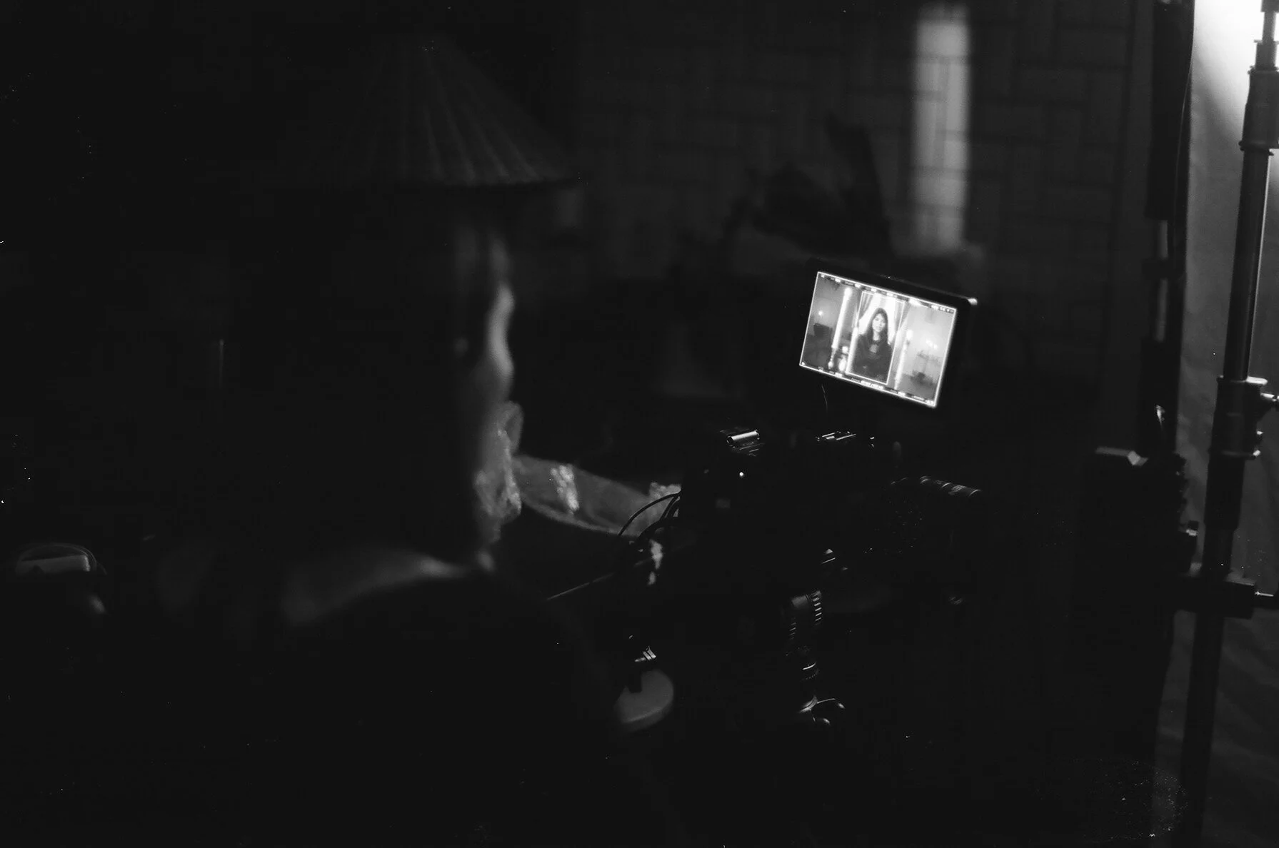 A person wearing headphones dials a smartphone camera, taking a photo of a woman on the screen, with studio lights and equipment visible in a dark environment.