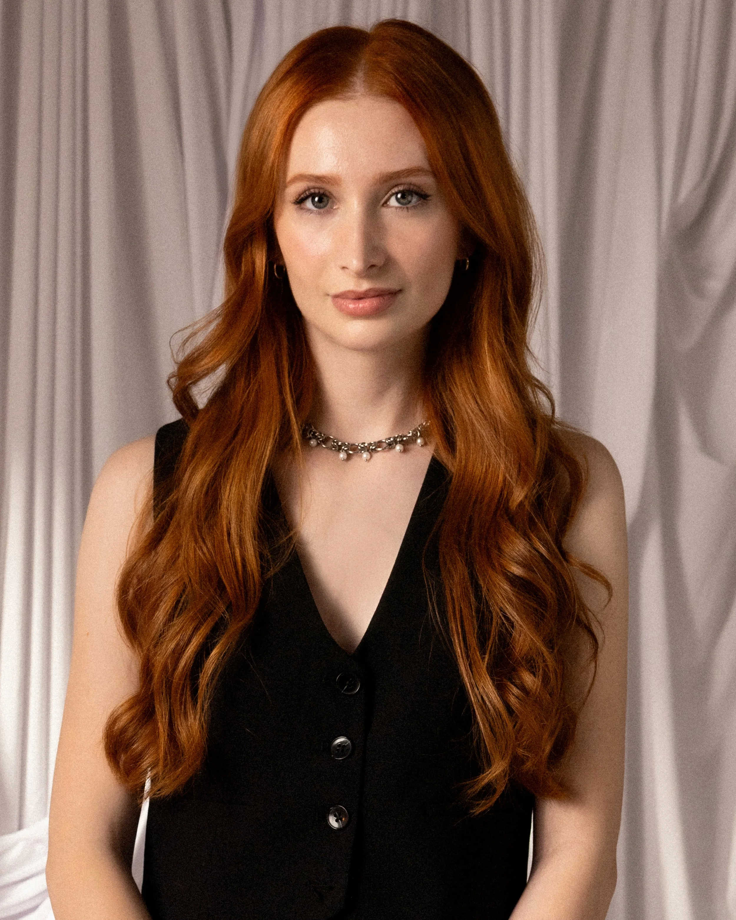 A person with long red hair wearing a black vest.