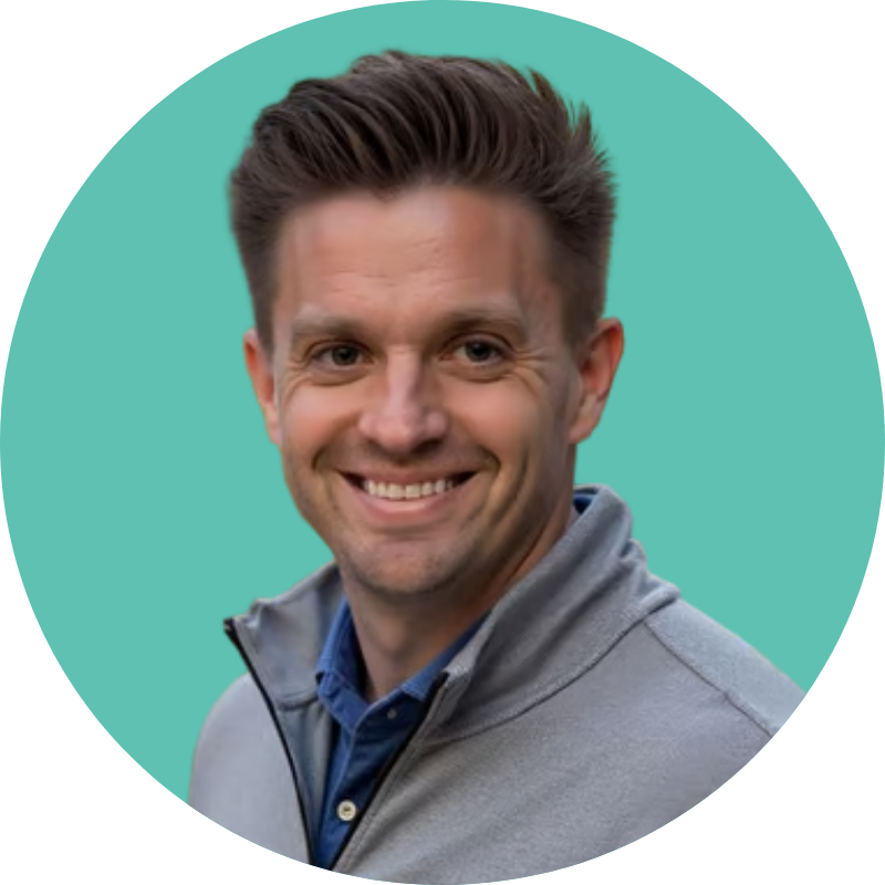 A smiling man with dark hair wearing a gray jacket over a blue shirt, standing against a teal background.