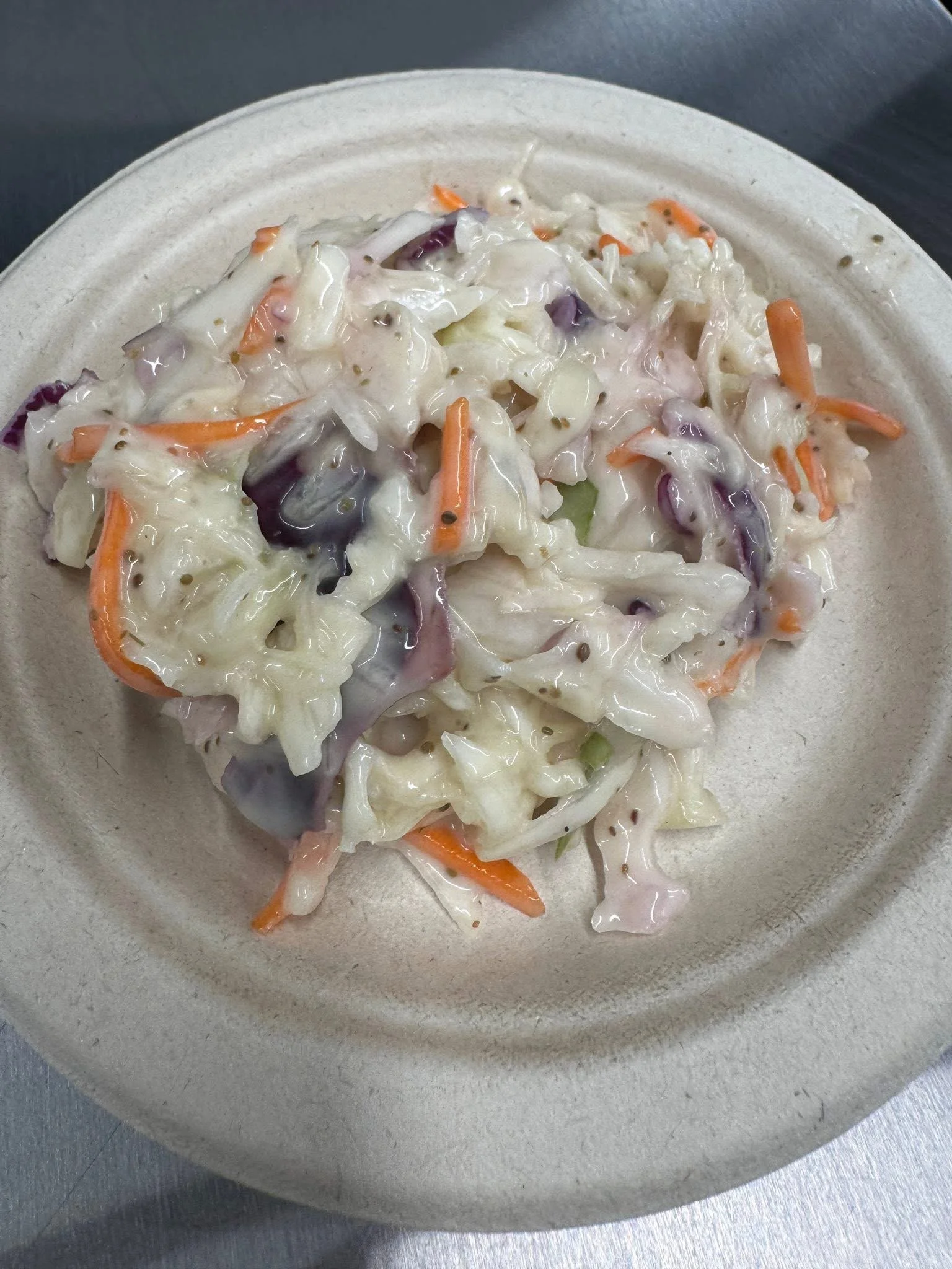 A paper plate with a serving of creamy coleslaw salad containing shredded cabbage, carrots, and purple cabbage.