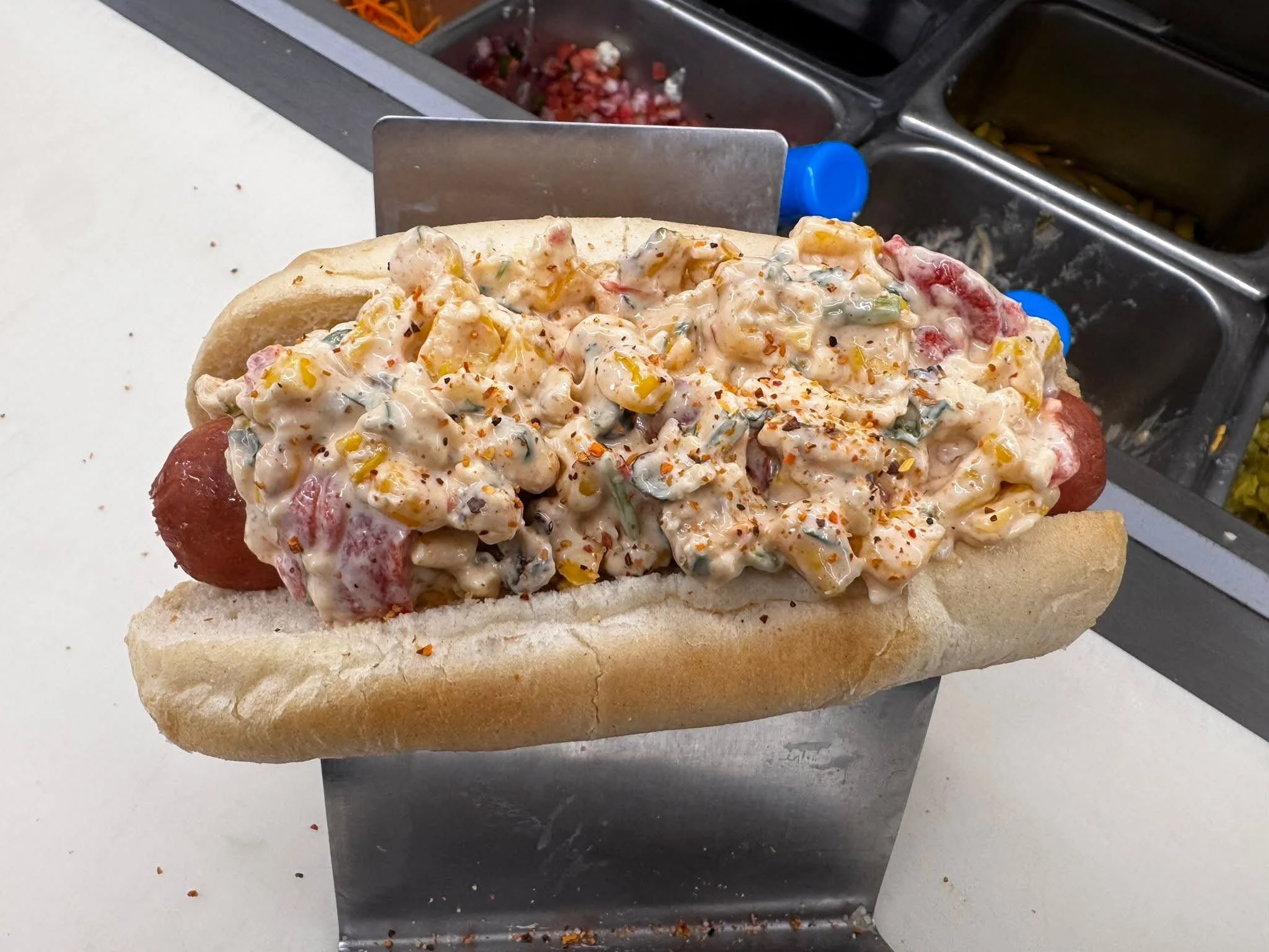 Hot dog with creamy potato salad topped with spices and served in a bun.