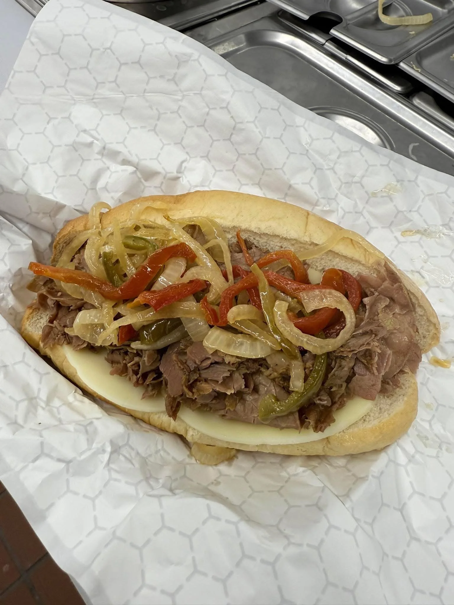 Philly cheesesteak sandwich with cooked beef, melted cheese, sautéed onions, and peppers in a hoagie roll.