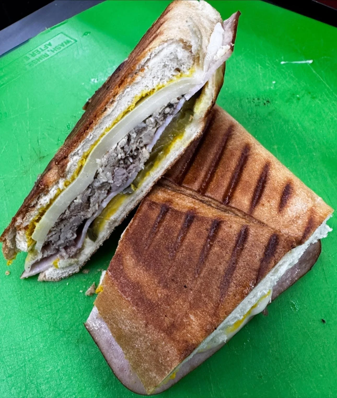 Grilled panini sandwich with cheese and turkey, cut in half, on a green cutting board.
