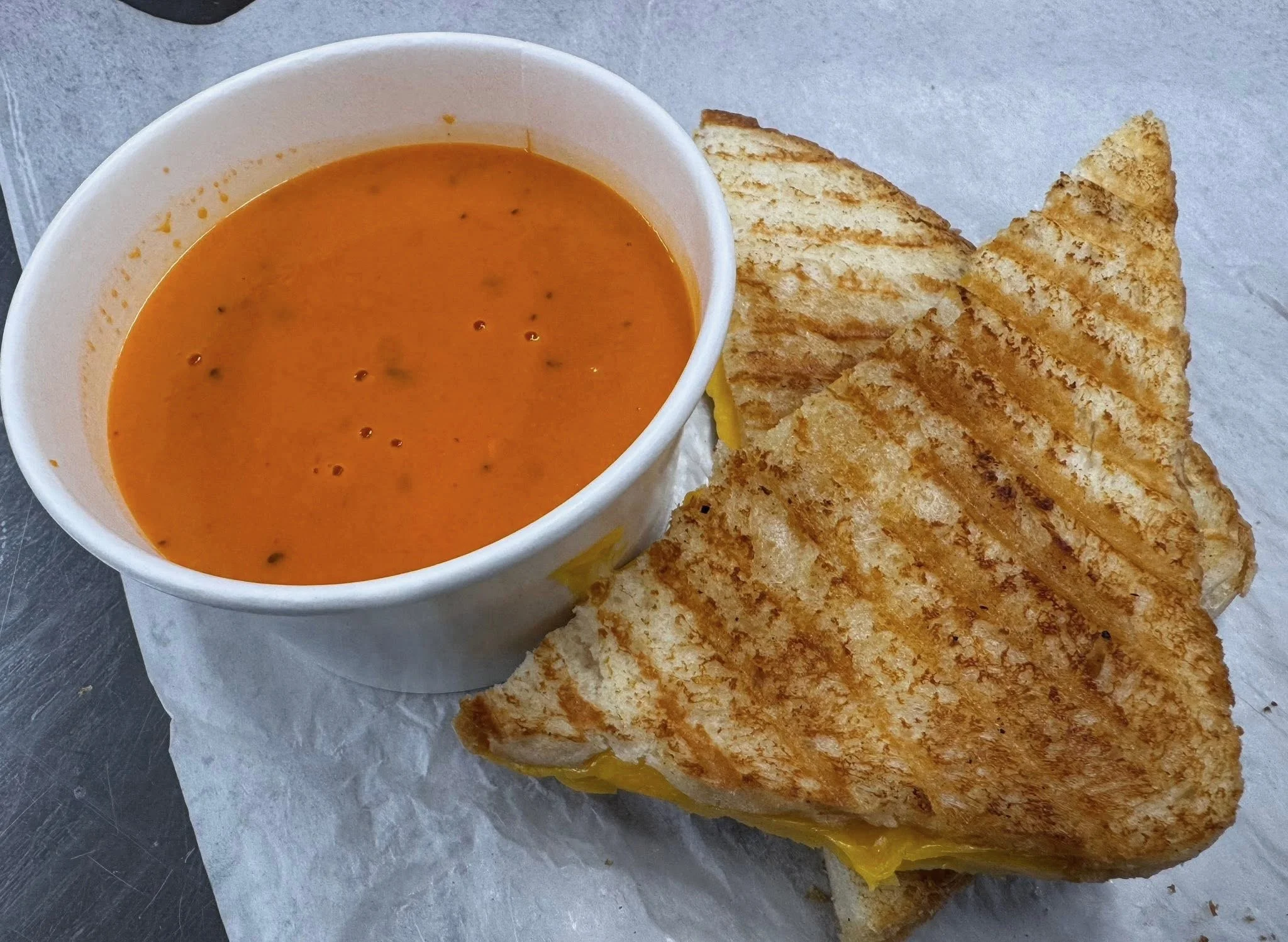 Grilled cheese sandwich with melted cheese and tomato soup served in a white cup.