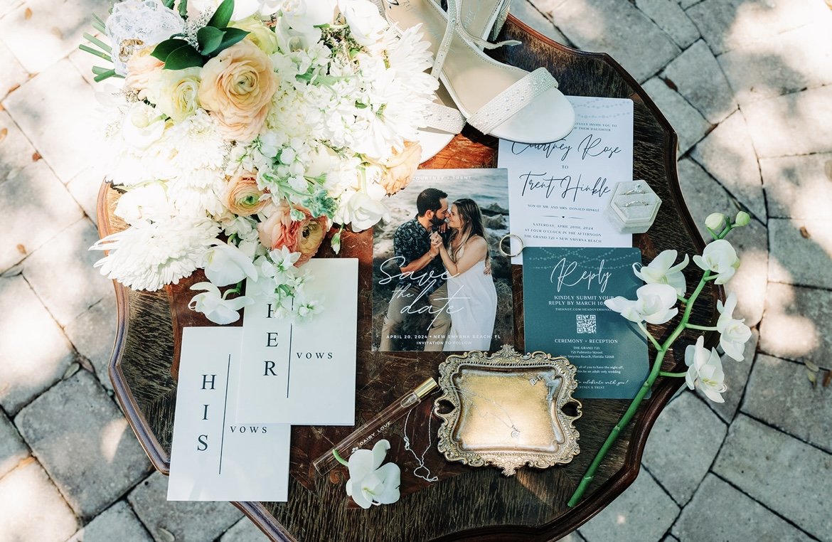 Wedding or engagement planning setup with flowers, a photo of a couple, invitation cards, a floral stem, and vintage tray on a wooden table.