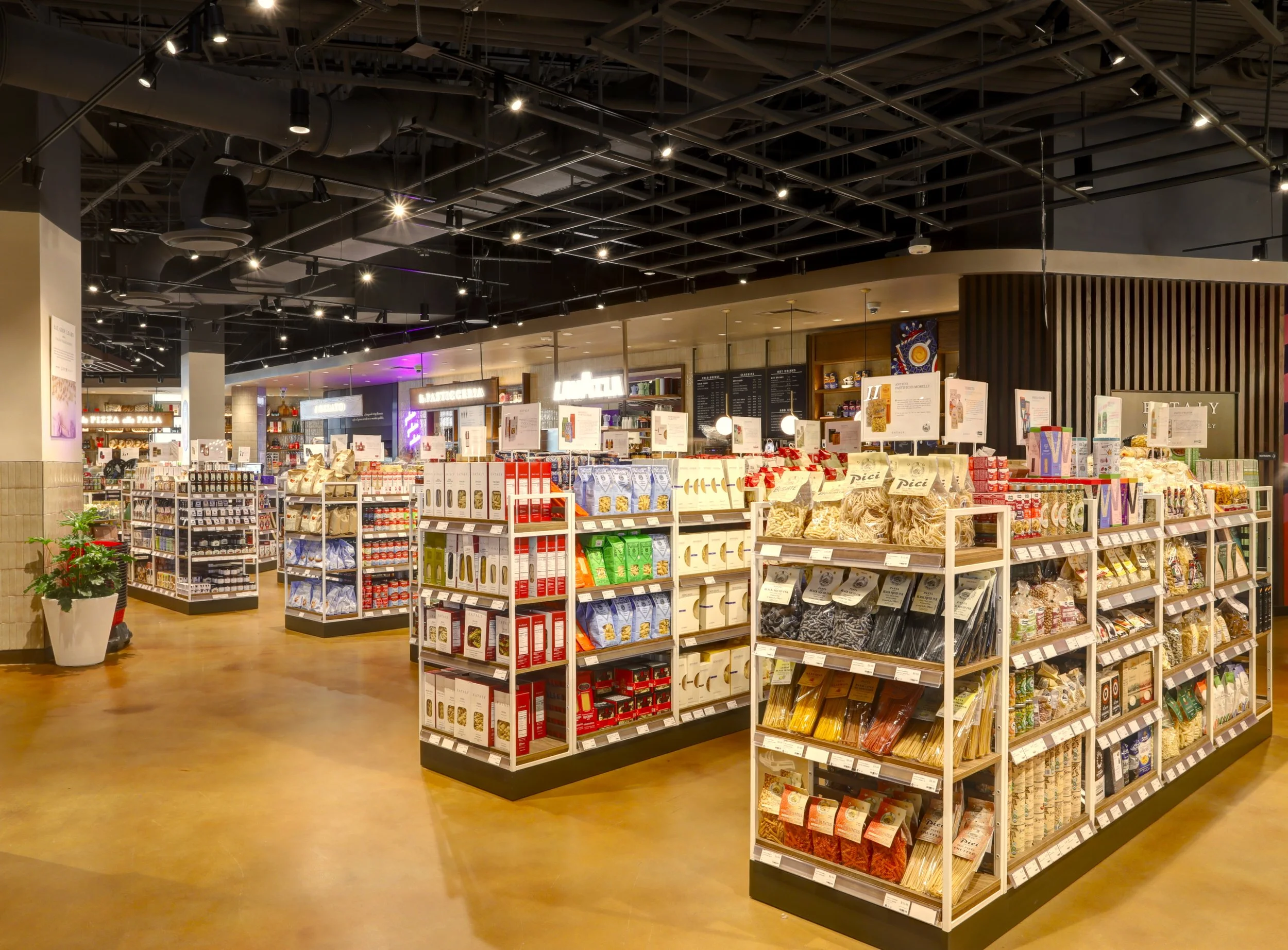 Interior view of a grocery store with shelves stocked with pasta, sauces, and other packaged foods, modern lighting, and a warm floor.