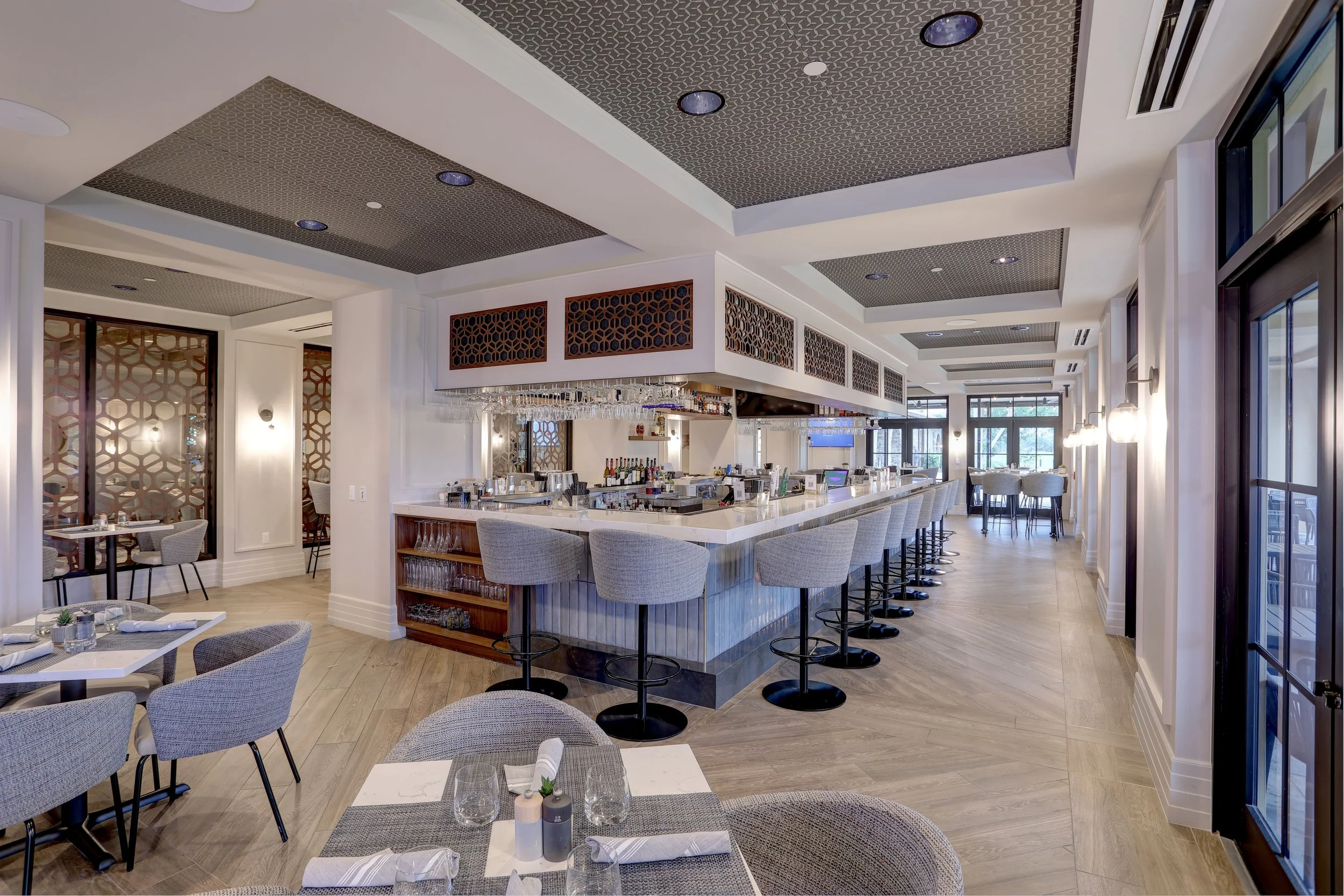 Modern restaurant interior with a bar counter, bar stools, and dining tables with chairs, well-lit with natural and artificial light.