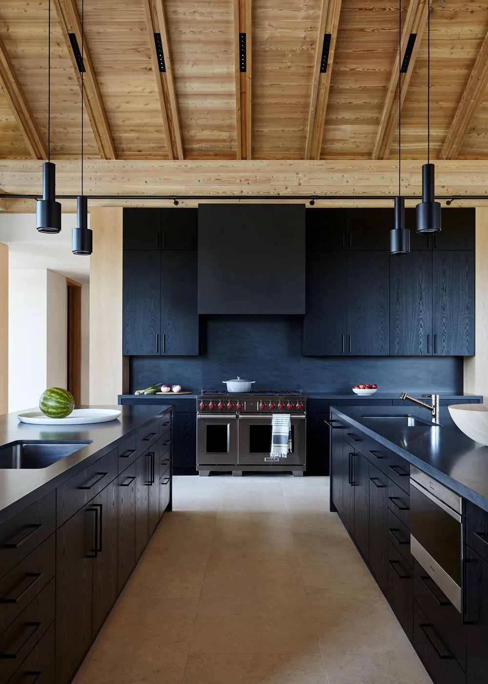 Modern kitchen with black cabinets, stainless steel stove, black countertops, wooden ceiling, and pendant lights.
