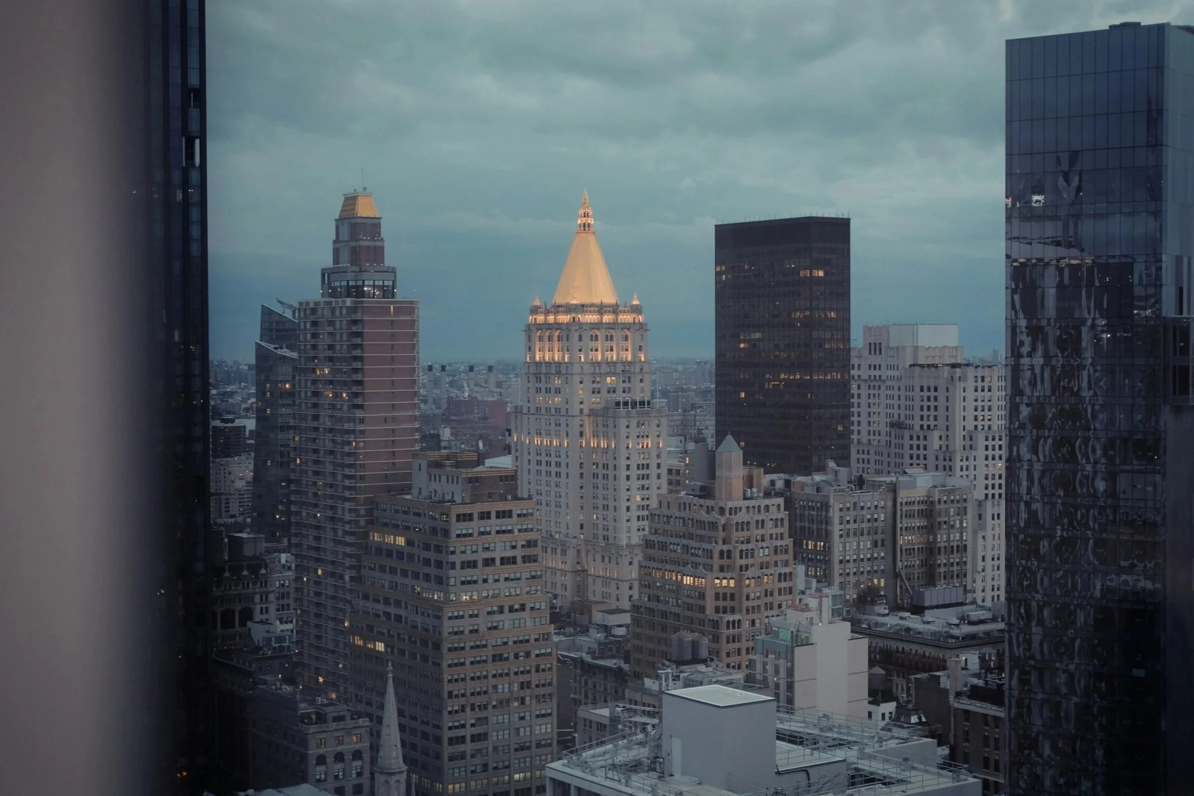 City skyline view with tall skyscrapers, including the prominent Empire State Building, during twilight with cloudy sky.