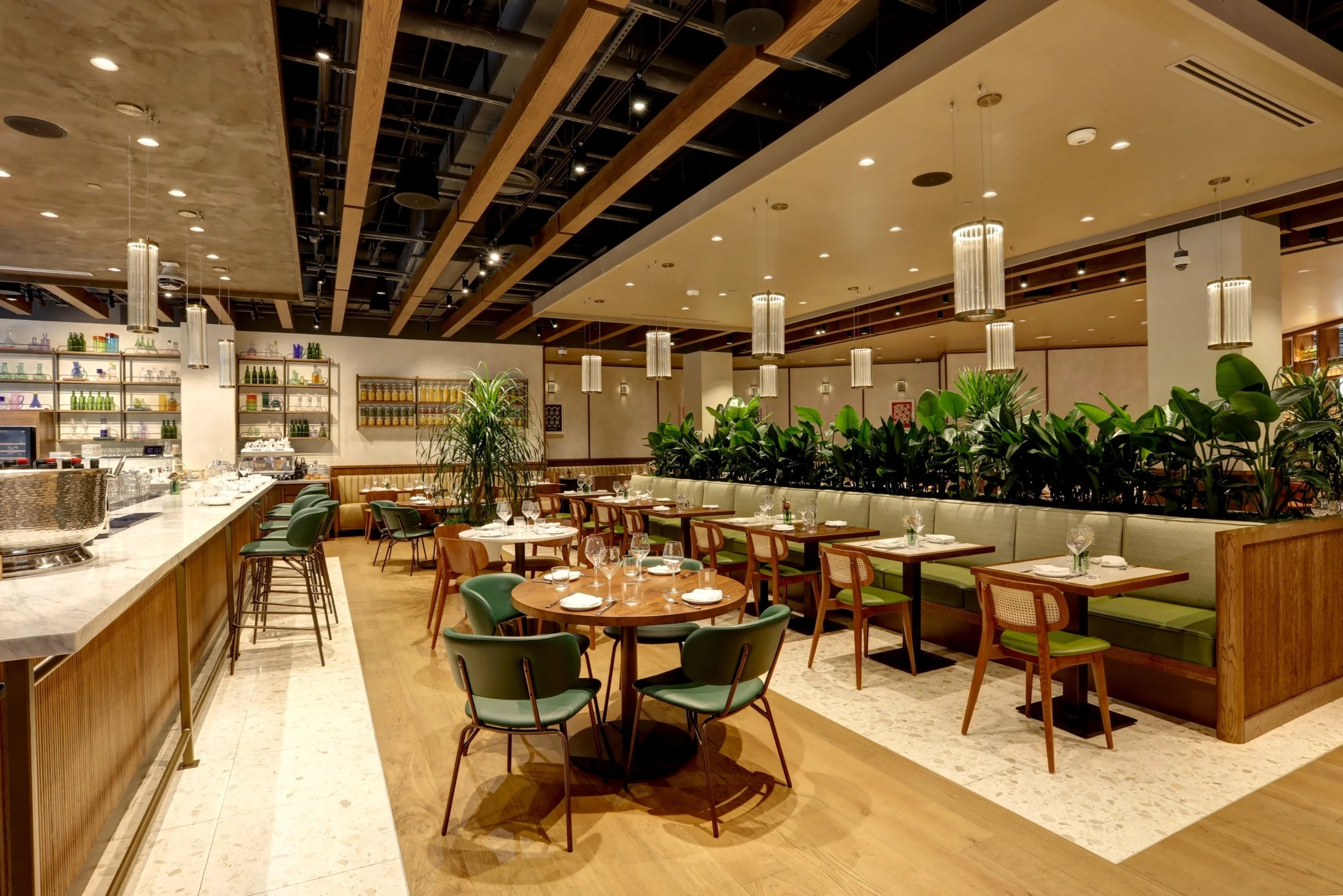 Elegant restaurant interior with wooden accents, green and white seating, plants, and hanging lights.