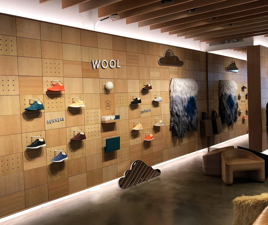 Display wall with colorful shoes, wool decorative elements, and cloud-shaped ornaments in a retail store.