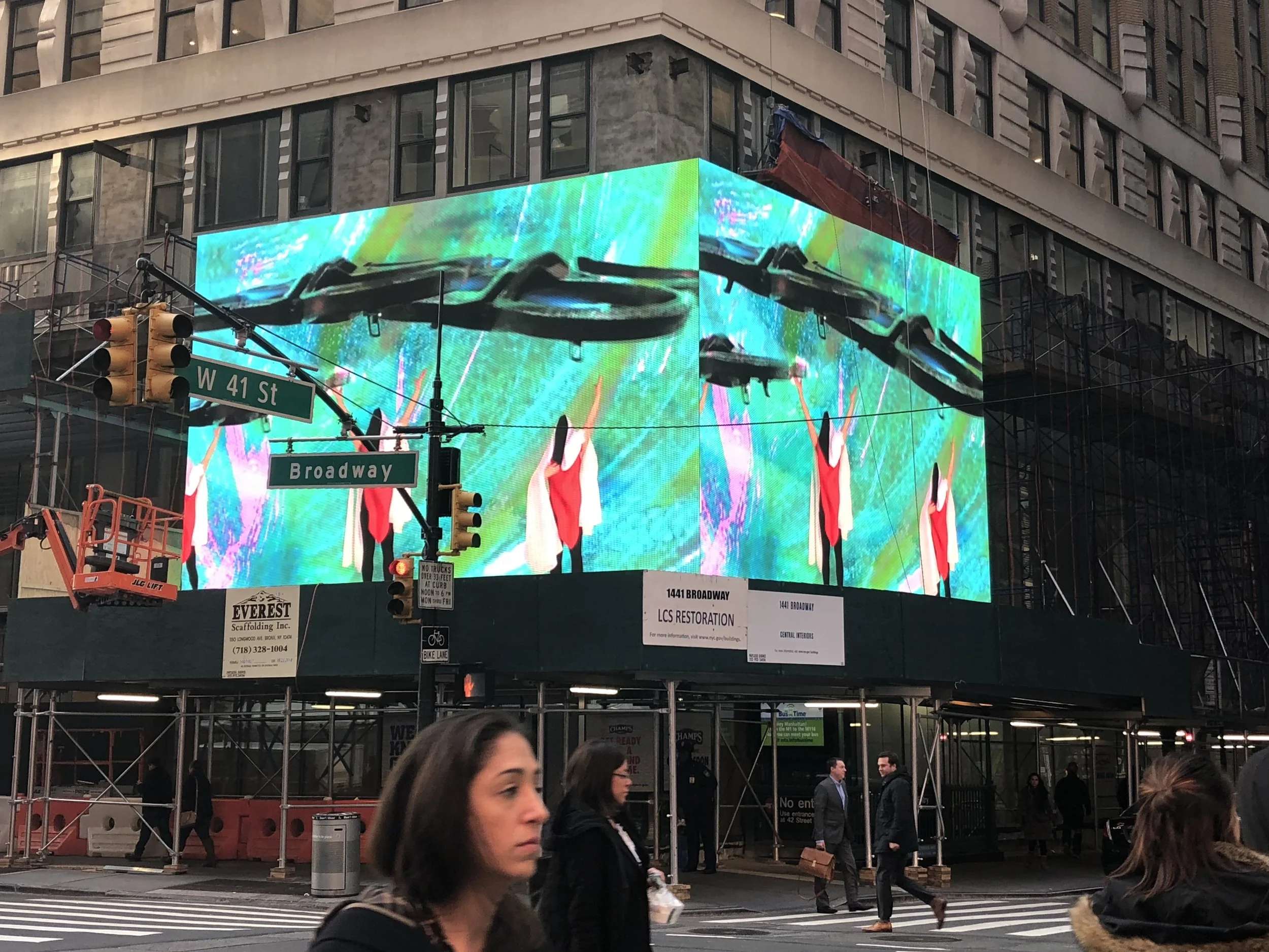Digital billboard showing a colorful, abstract background with several dancers in red and white costumes performing.