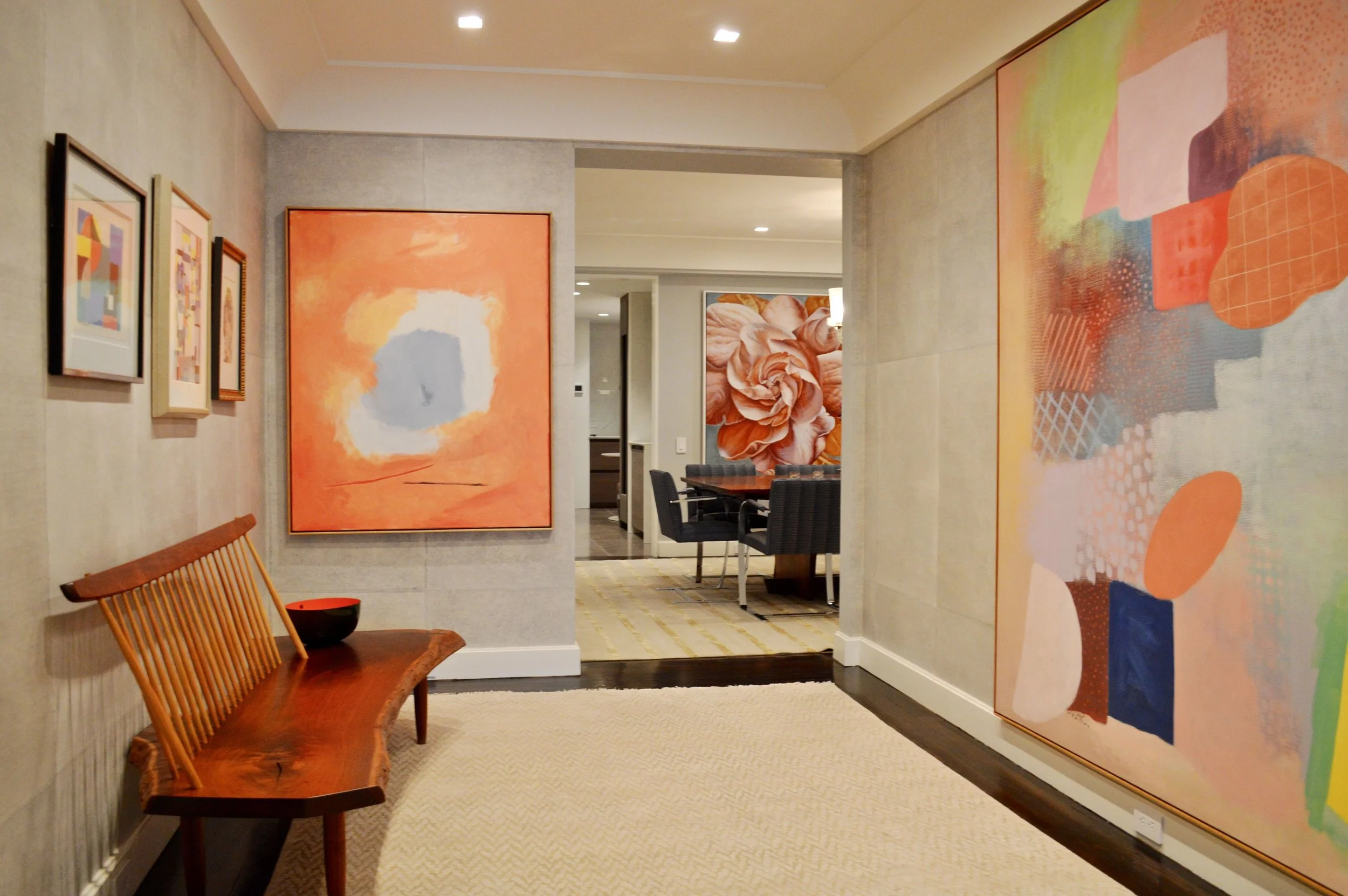 Interior of a modern art gallery featuring colorful abstract paintings on the walls, a wooden bench, and a dining area in the background.