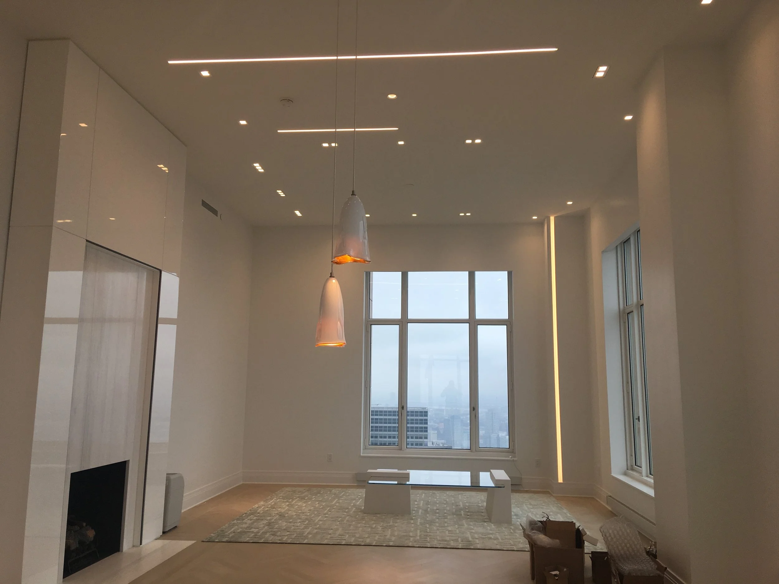 Modern living room with high ceilings, large window, minimal furniture, and pendant lights.