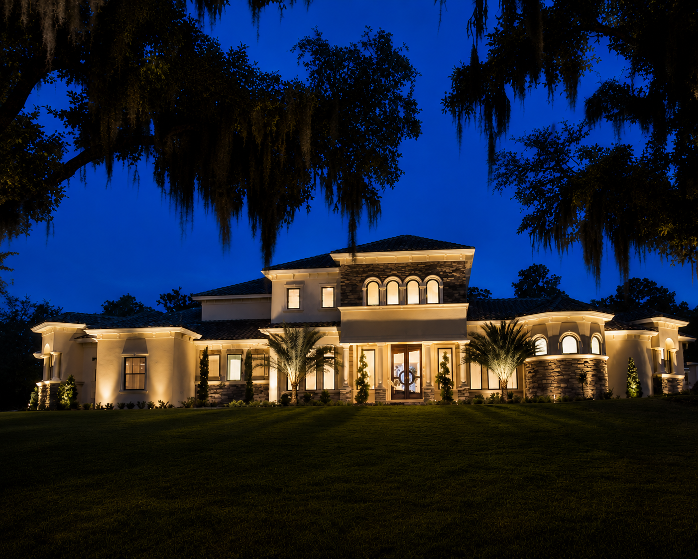 A large, illuminated luxury house at night. Landscape lighting example by Vibe Lighting