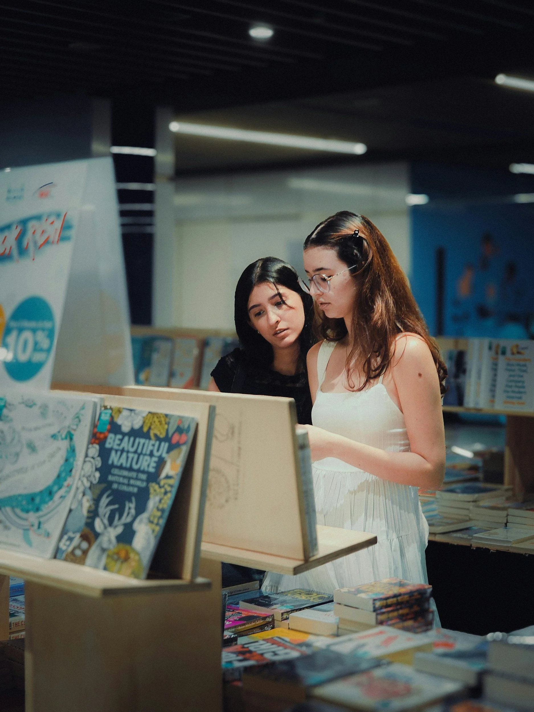 Two women shopping for books at a bookstore, with one woman looking at a book and the other standing nearby.