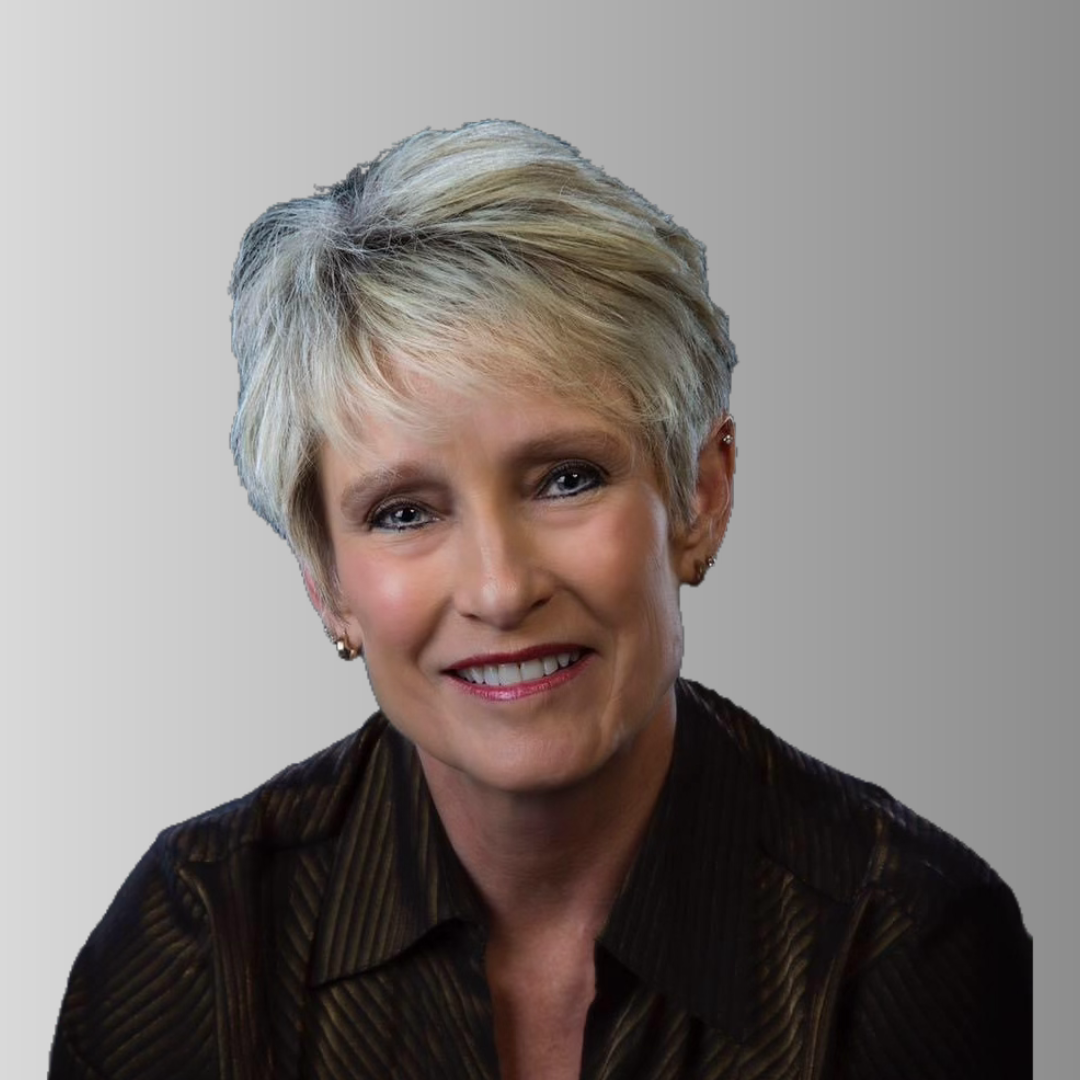 Headshot of woman with short blonde hair, wearing a dark striped shirt, against a plain light gray background.