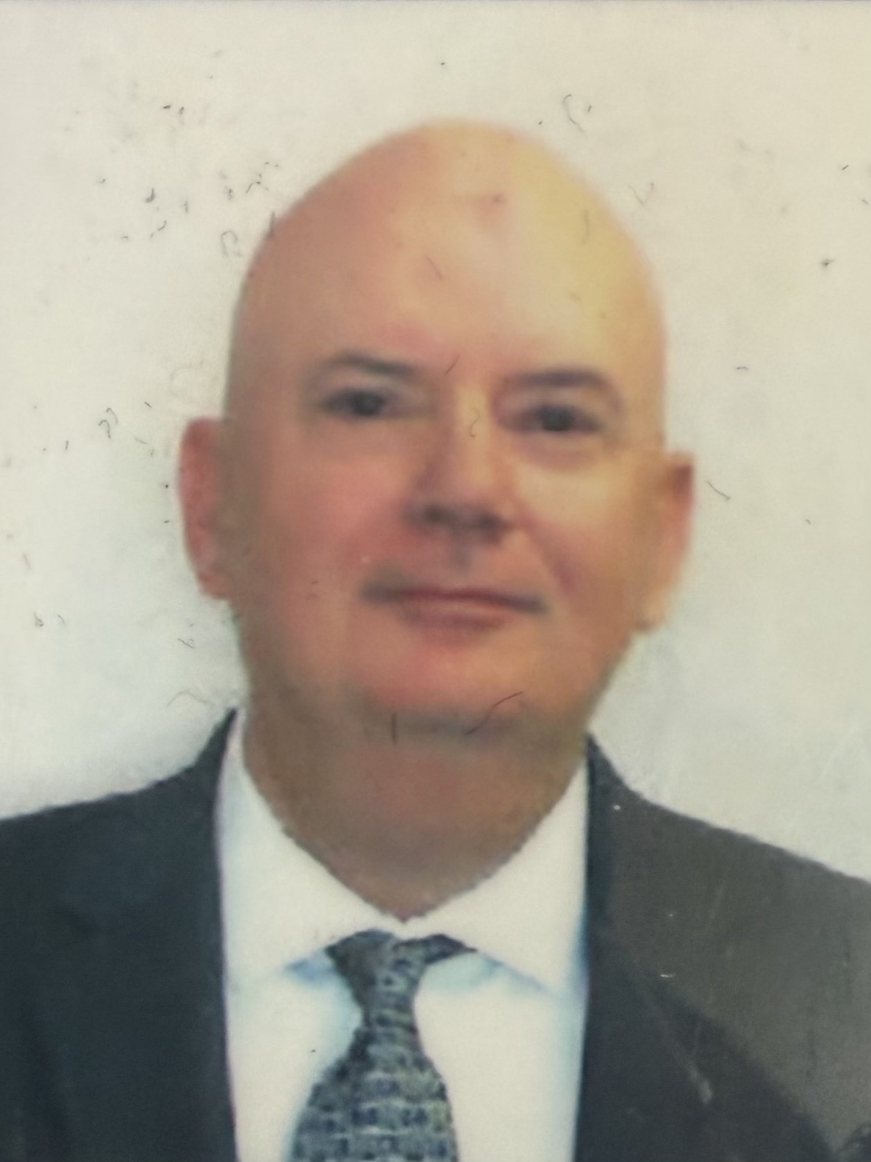 A man in a suit, white shirt, and patterned tie, with a light background.