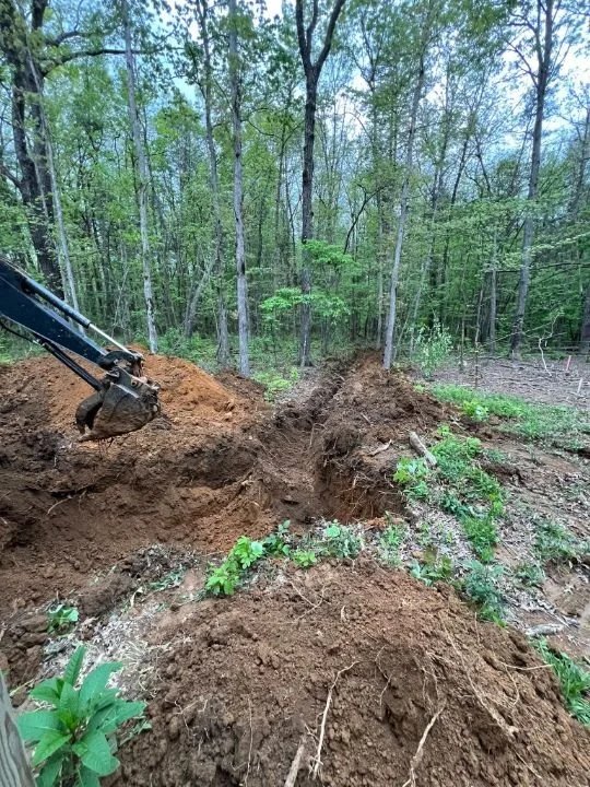 Excavator digging a trench for underground utilities on a wooded property in Altamont, TN