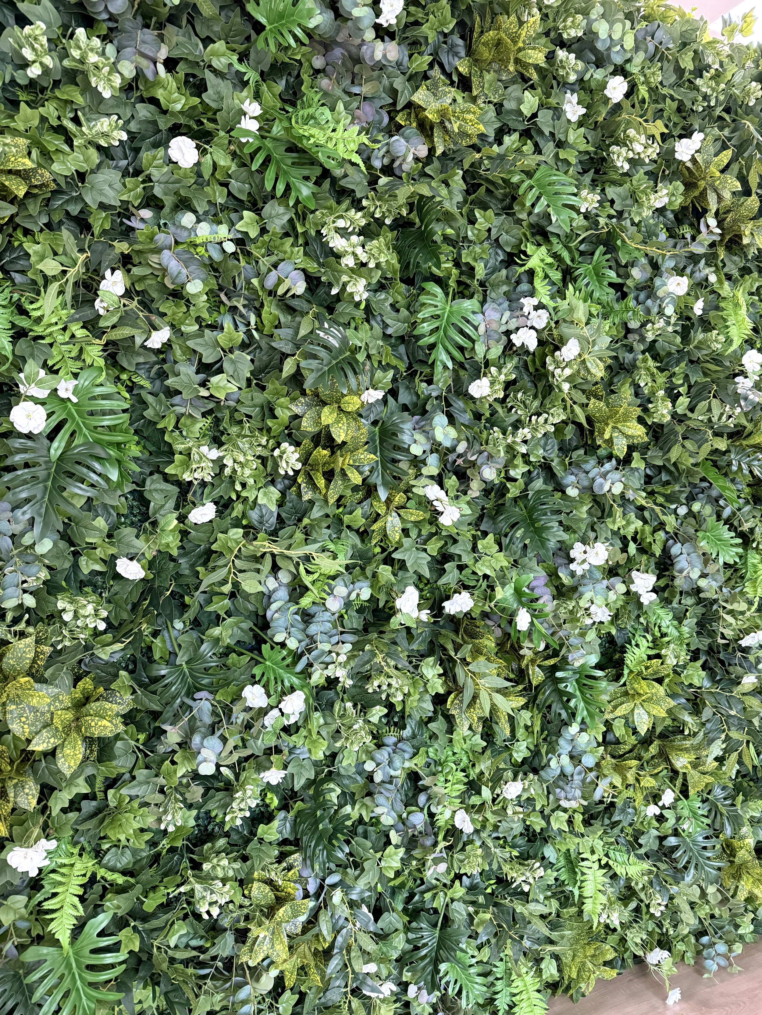 Rich mixed greenery, layered tropical leaves, scattered white blooms.