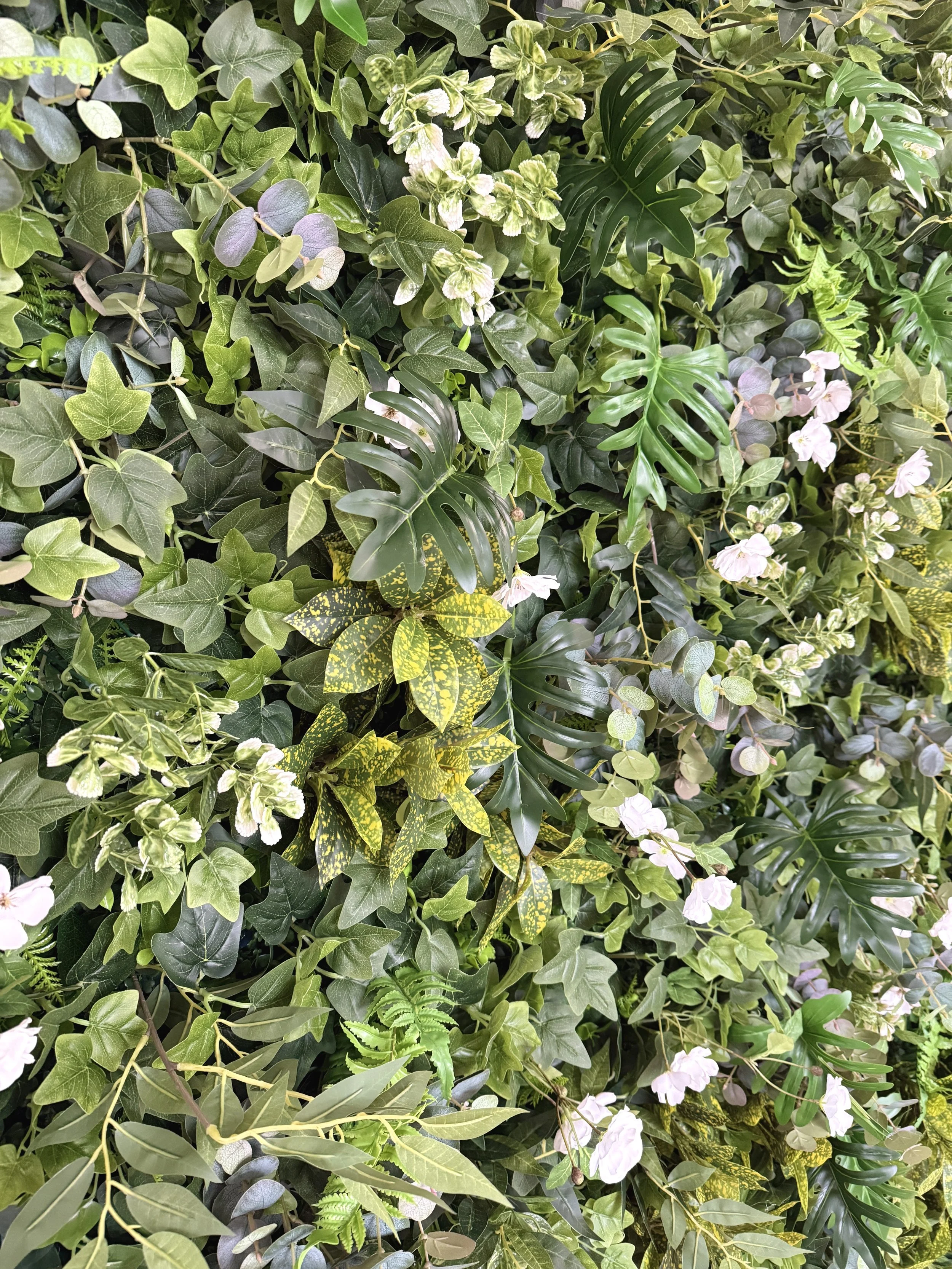 Rich mixed greenery, layered tropical leaves, scattered white blooms.