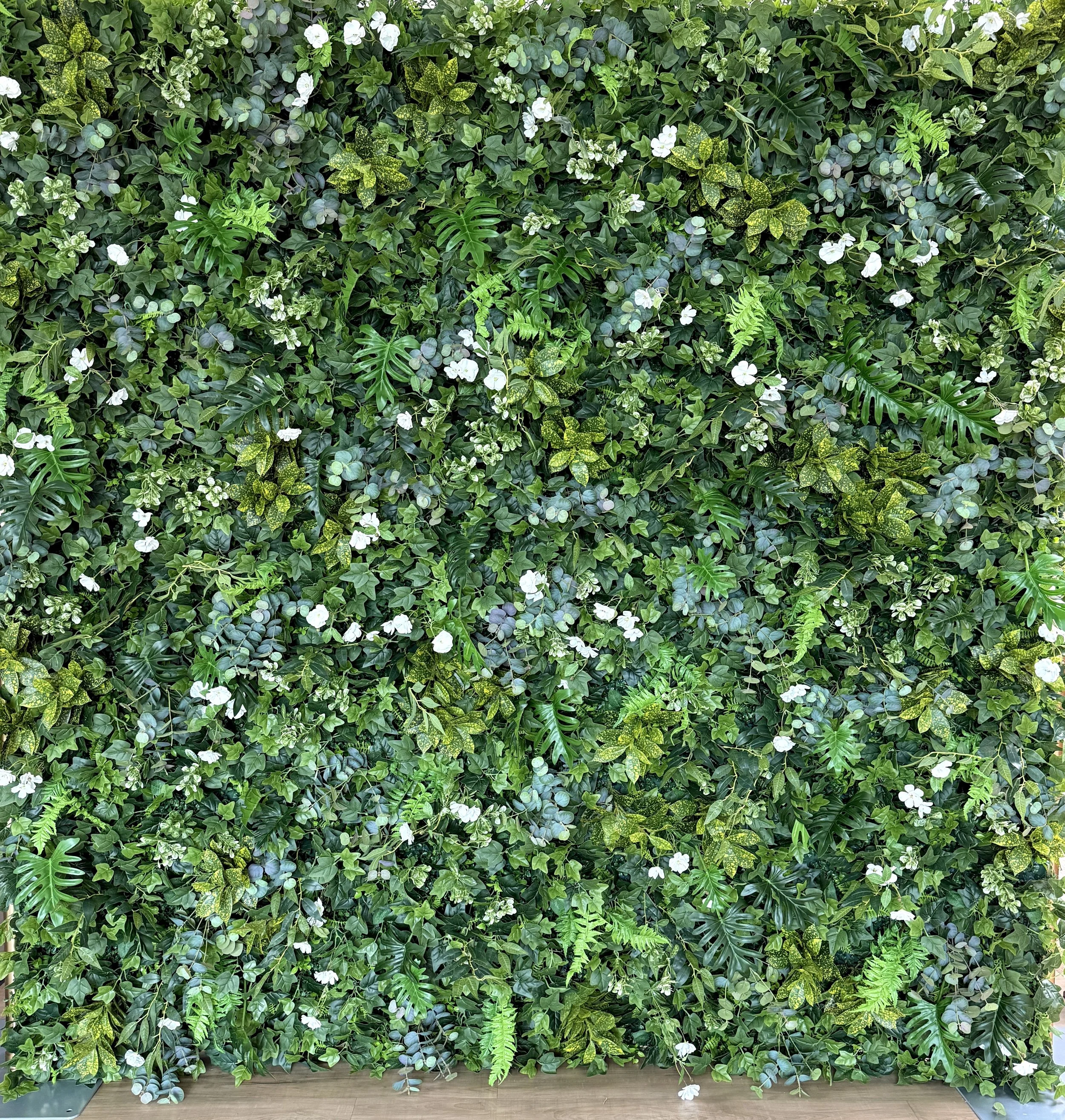 Rich mixed greenery, layered tropical leaves, scattered white blooms.