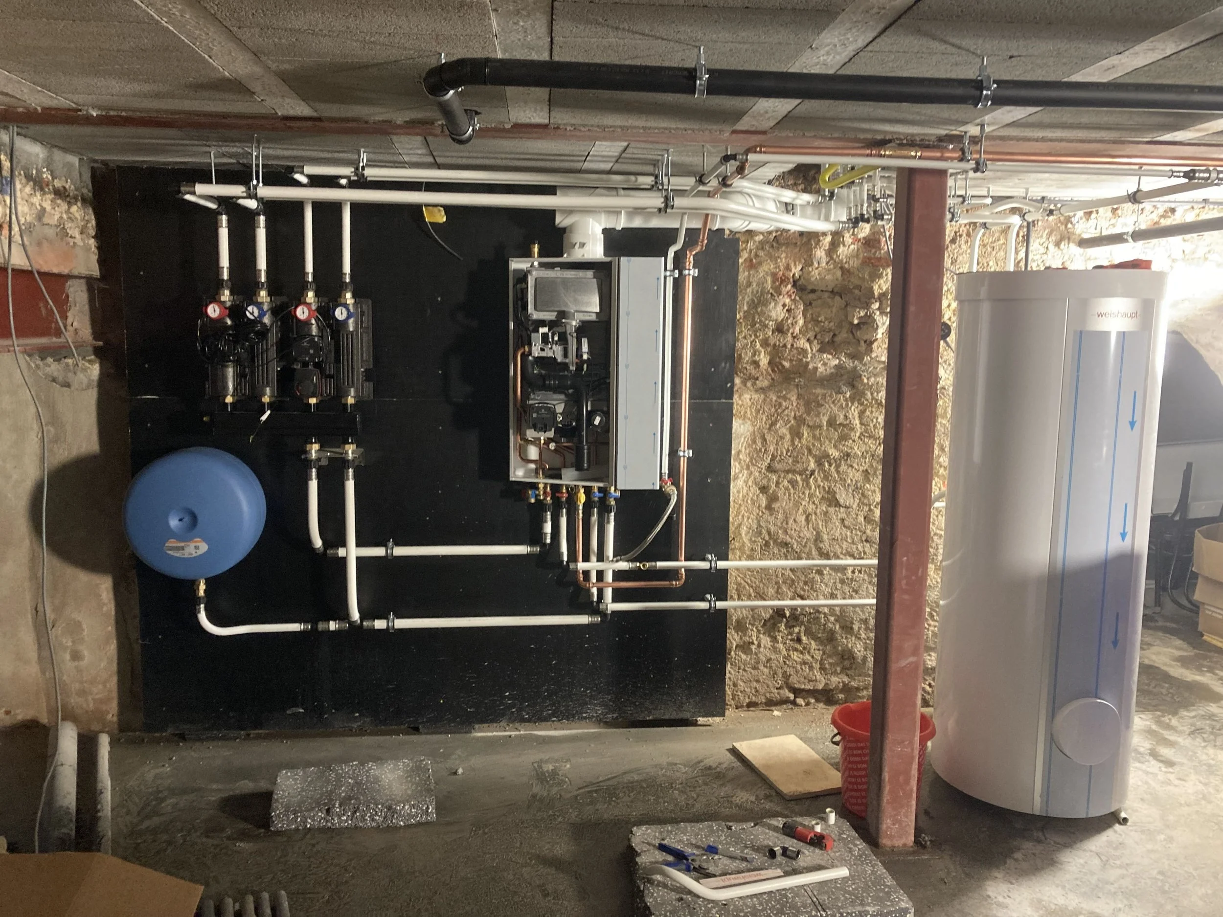 Installatie met pompen, leidingen, een drukvat en een warmwaterboiler in een kelder of ondergrondse ruimte.