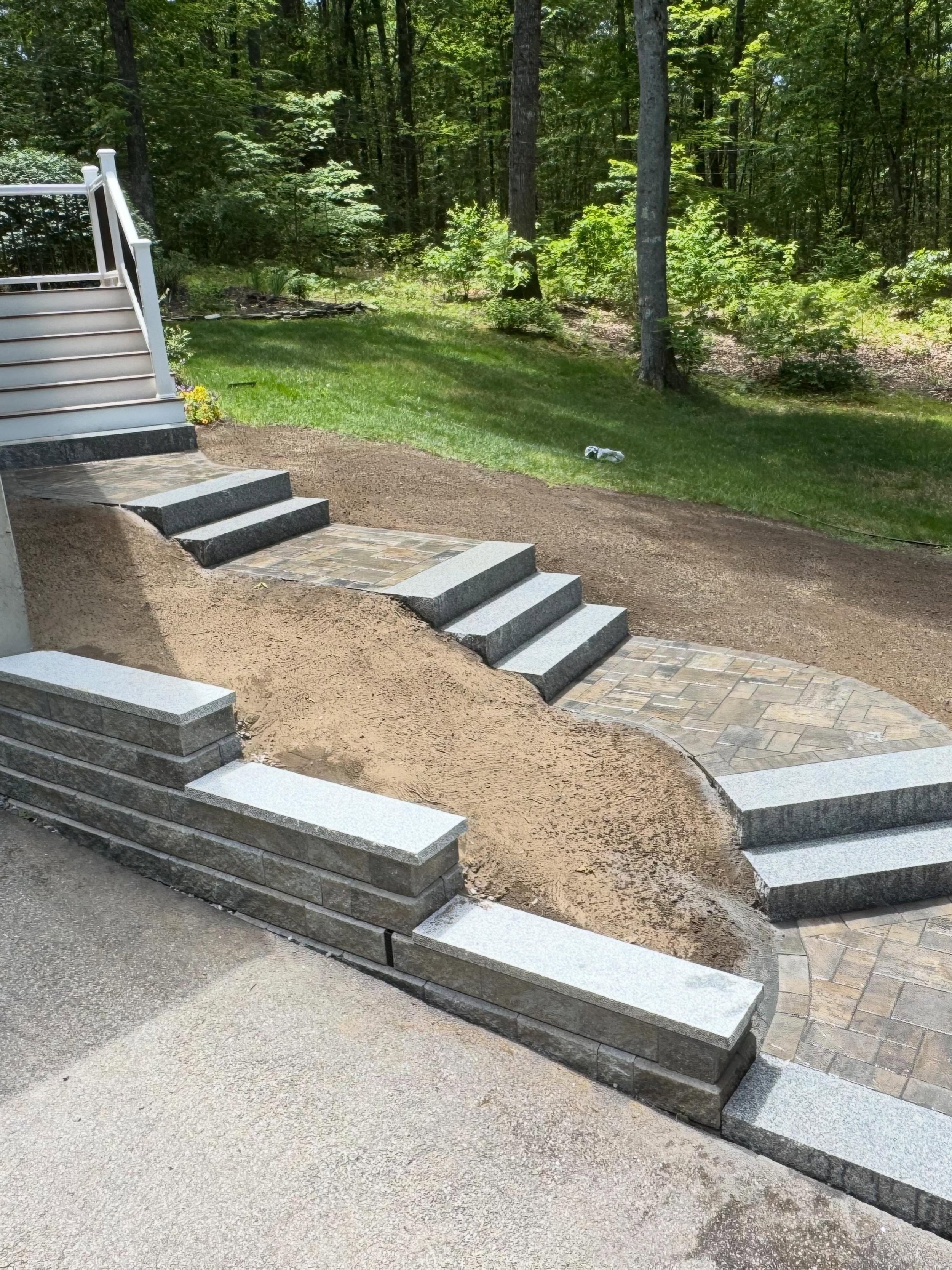 View a completed retaining wall and walkway installation in Chester, NH featuring Unilock Treo Premier pavers, Concord wall block, Almond Grove color, and granite accents.