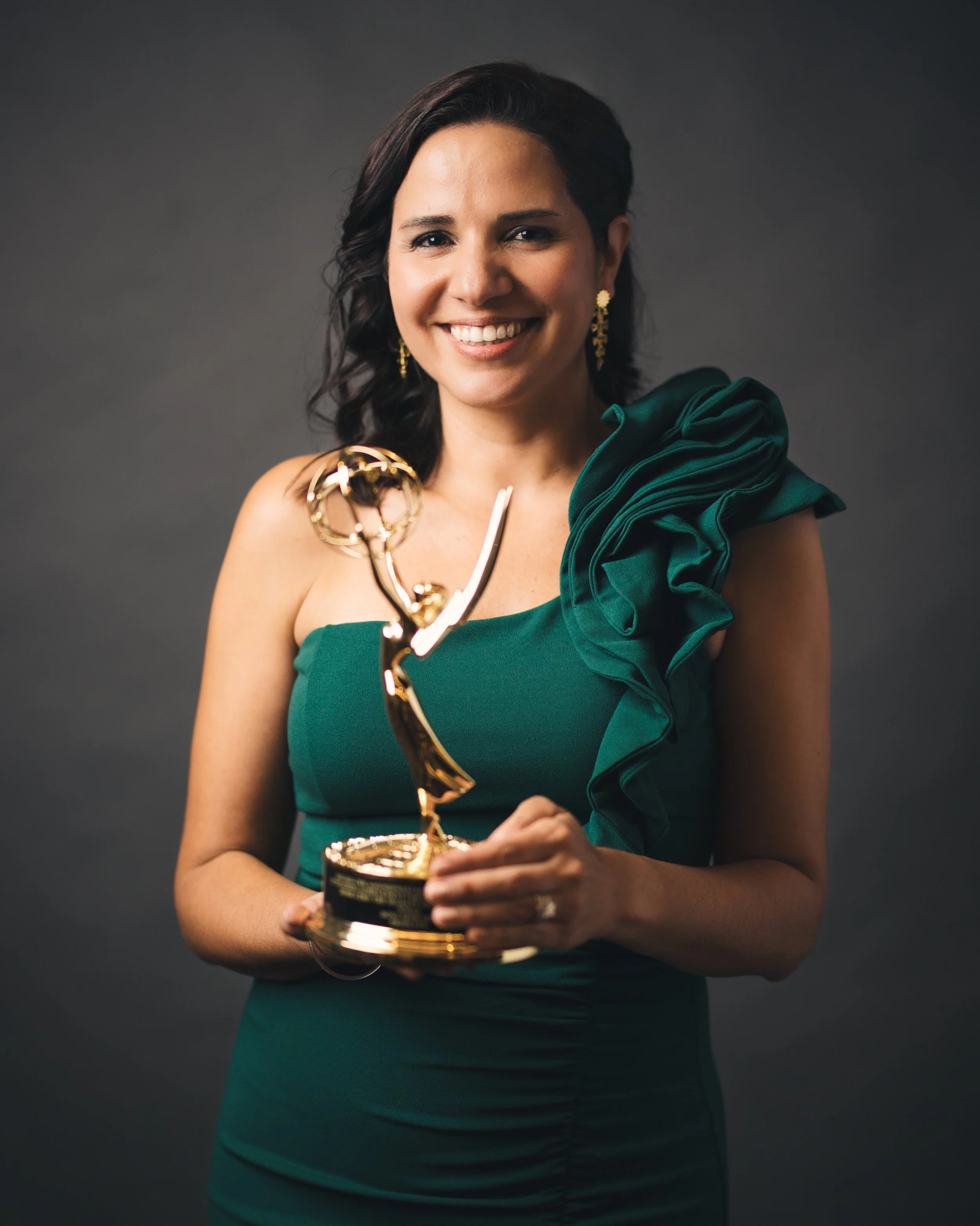 Woman in green dress holding an award statue, smiling, with dark background.