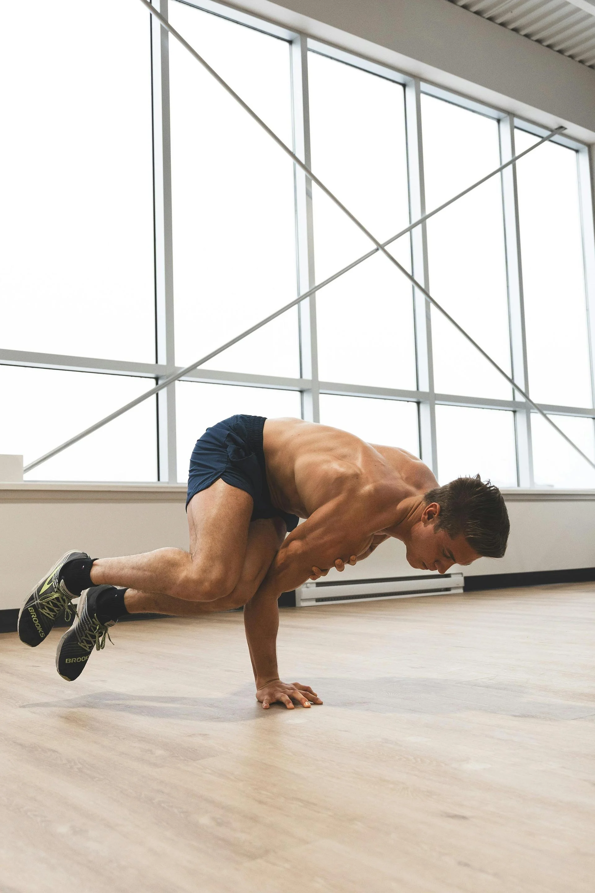 Person performing a yoga pose in a fitness studio with large windows.