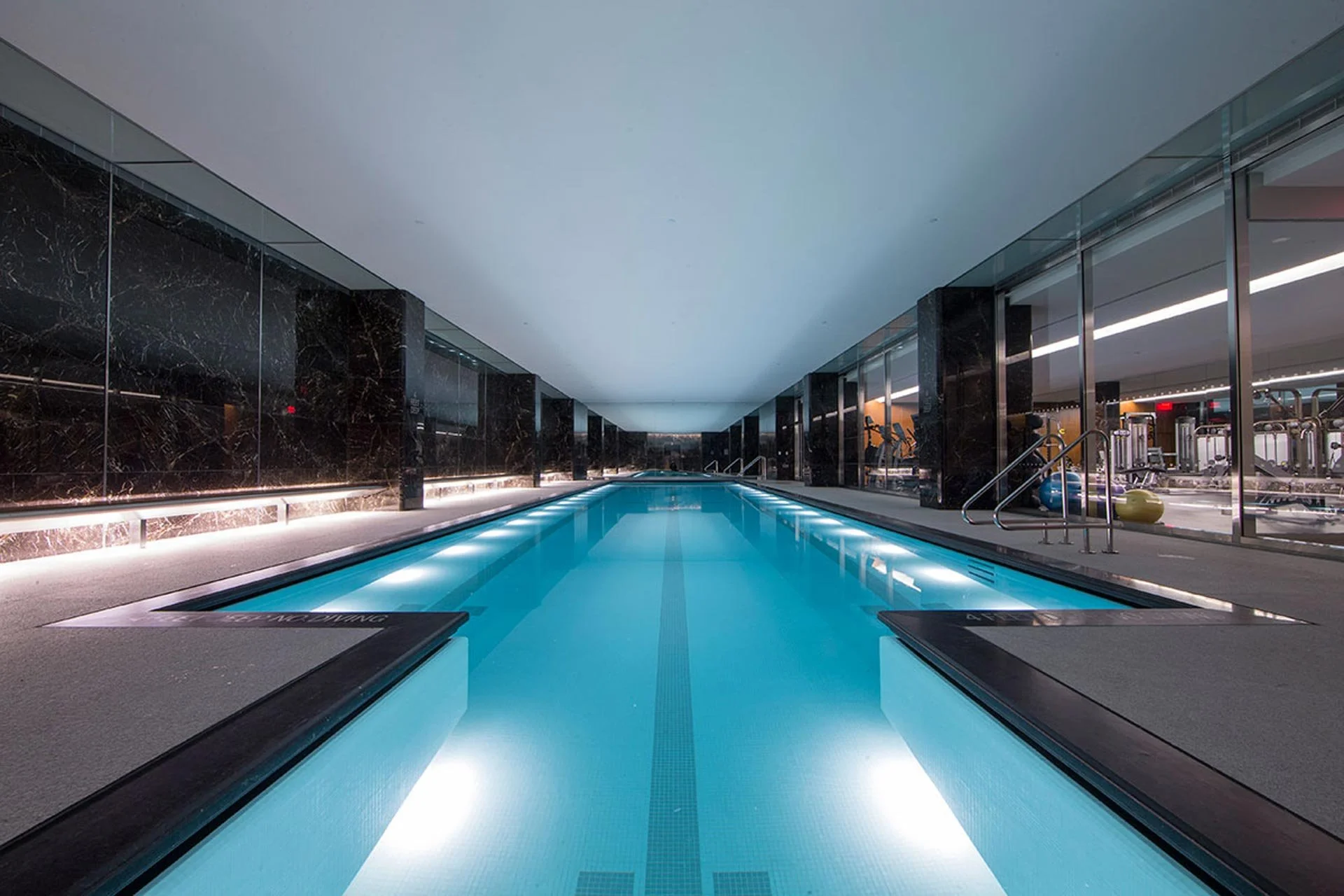 Indoor swimming pool with gym equipment visible through glass walls