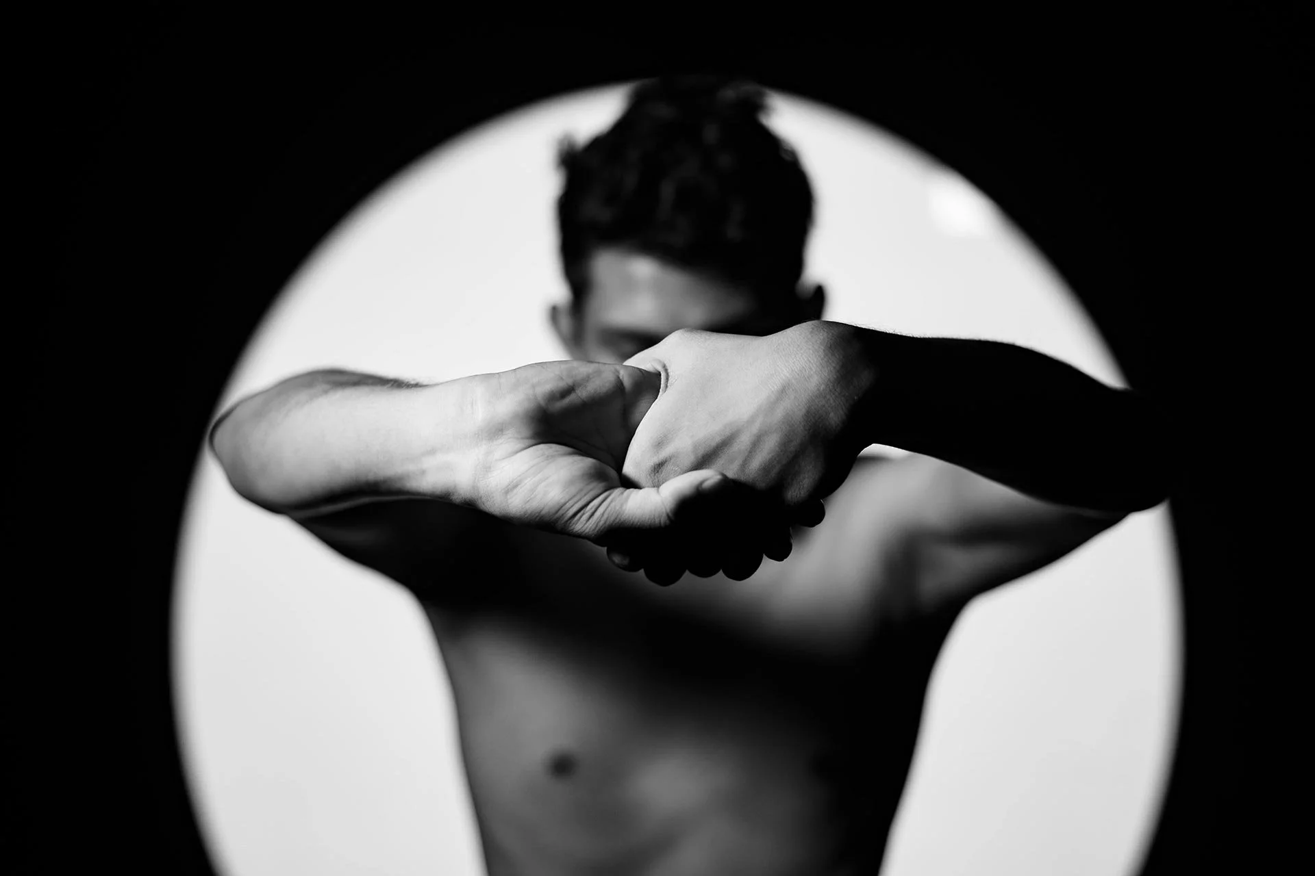 Black and white photo of a person with arms extended, hands clasped together, obscuring their face.