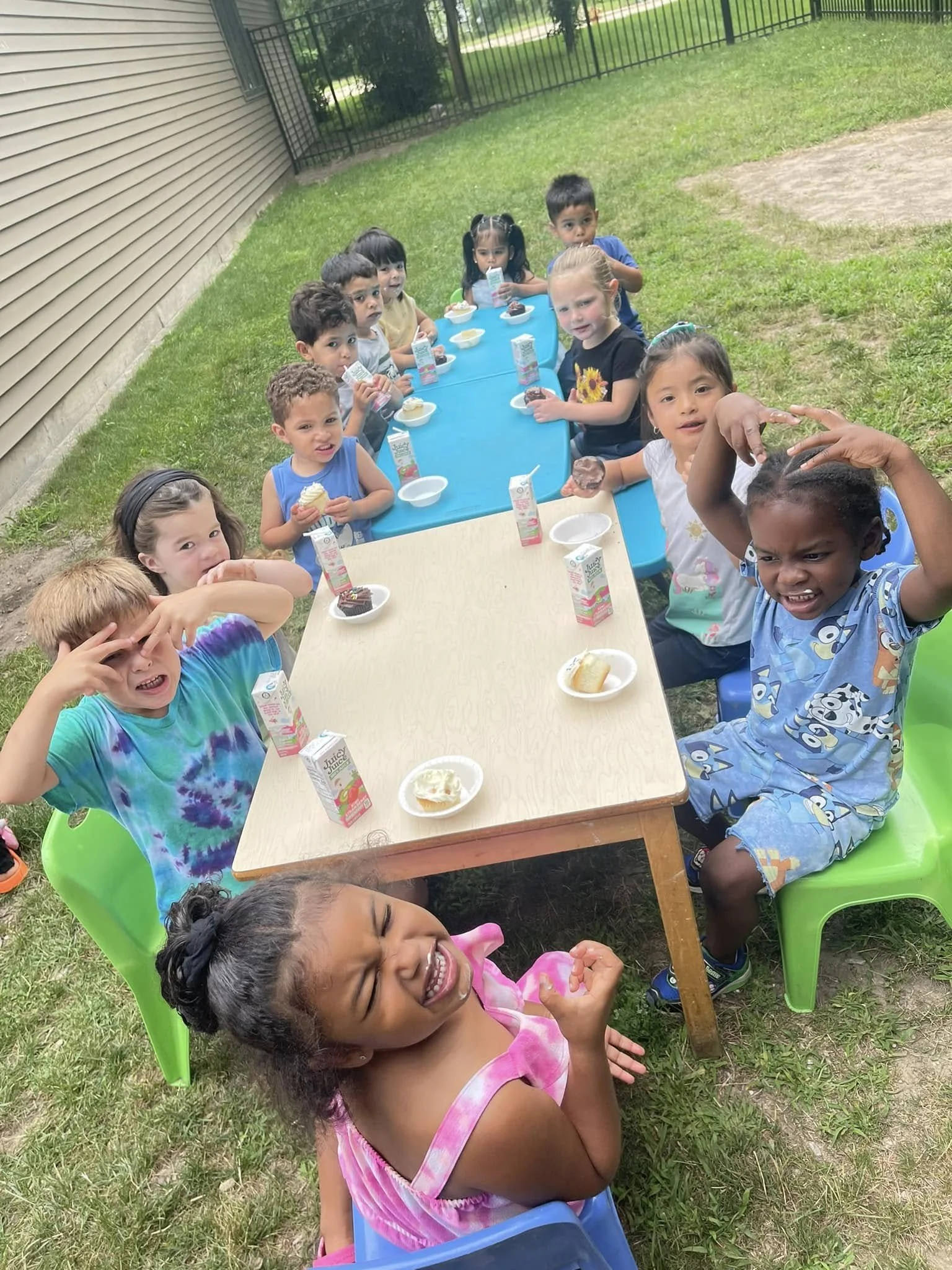 Children sitting at tables outside with snacks and juice boxes during a celebration or snack time.