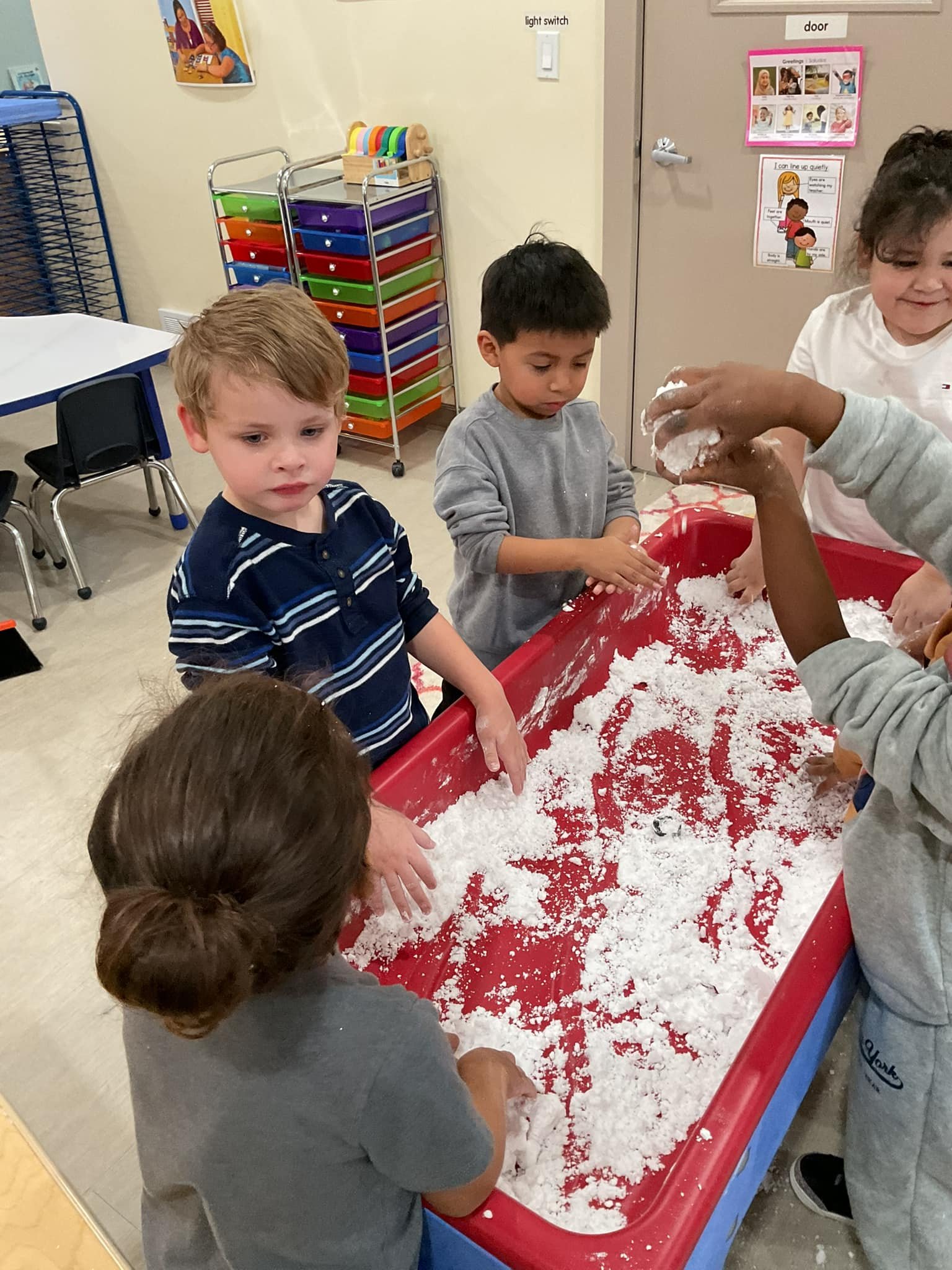 Children playing with white sensory or moon sand in a red tray in a classroom.