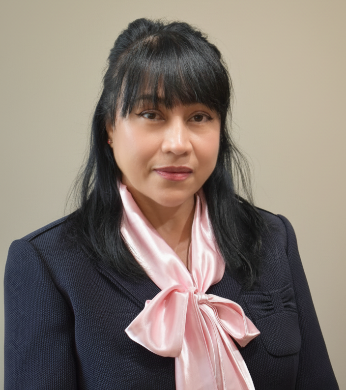 A woman with black hair and bangs wearing a black blazer and a pink satin bow tie shirt.